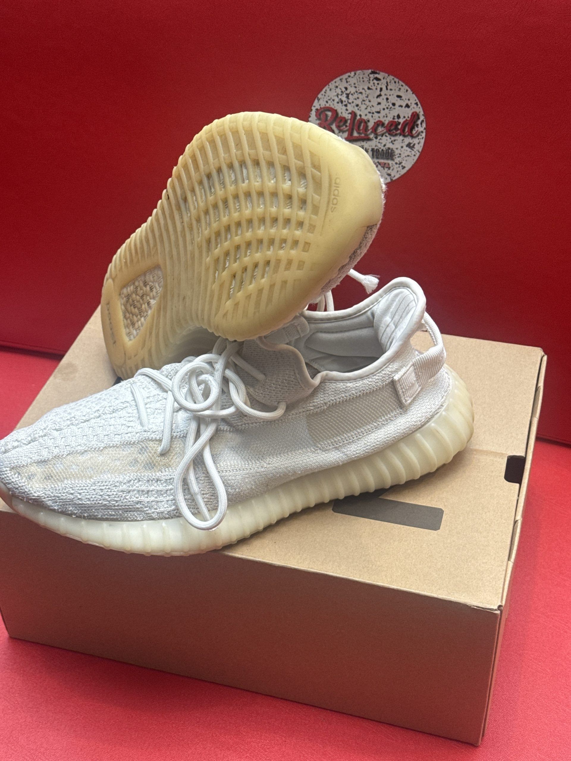 White Yeezy Boost 350 V2 sneakers with a tan sole and shoebox on a red surface.