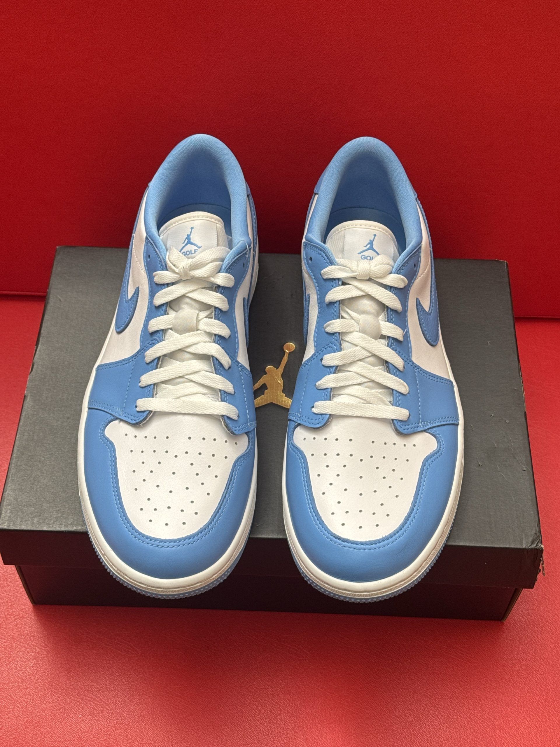 Light blue and white Air Jordan 1 Low sneaker sits on a black box, sole visible above.