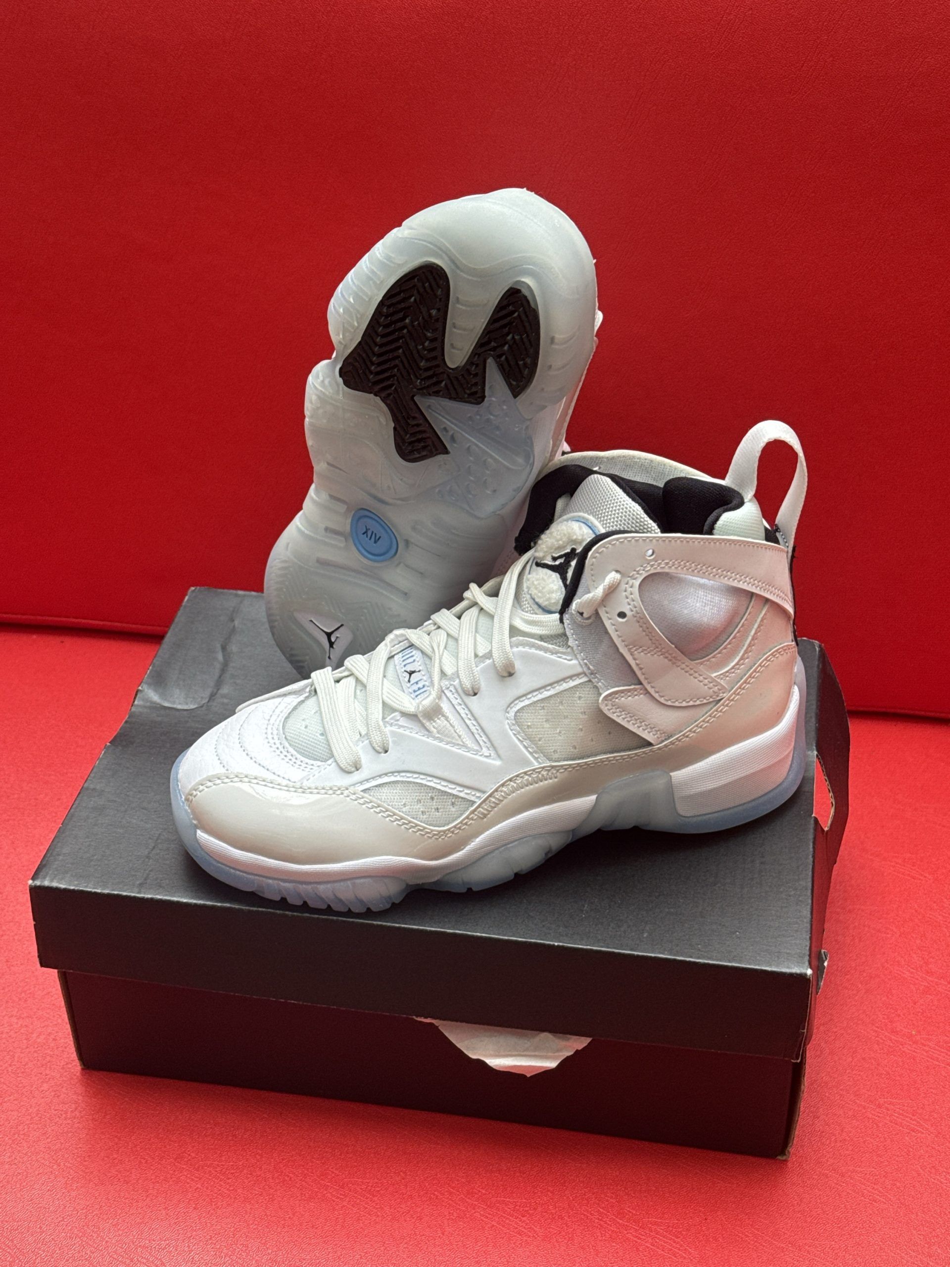 White and light blue Air Jordan shoes on a black box, set against a red background.