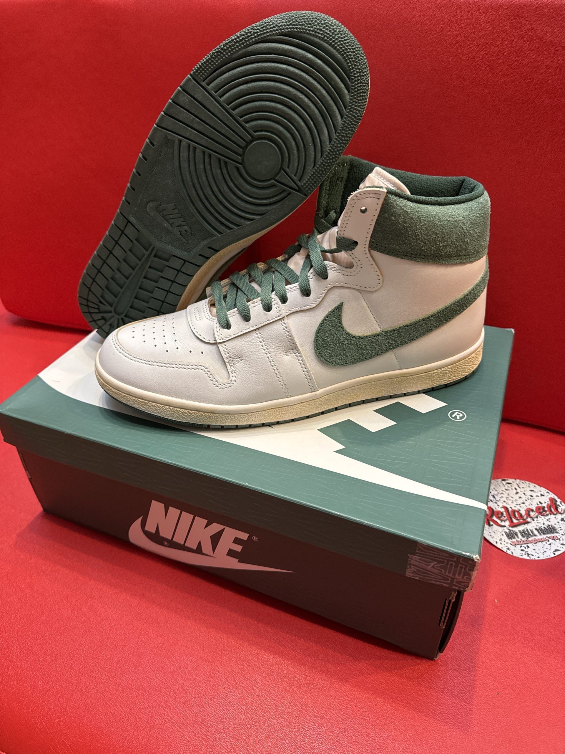 Pair of white and green Nike high-top sneakers with box and sole displayed on a red surface.