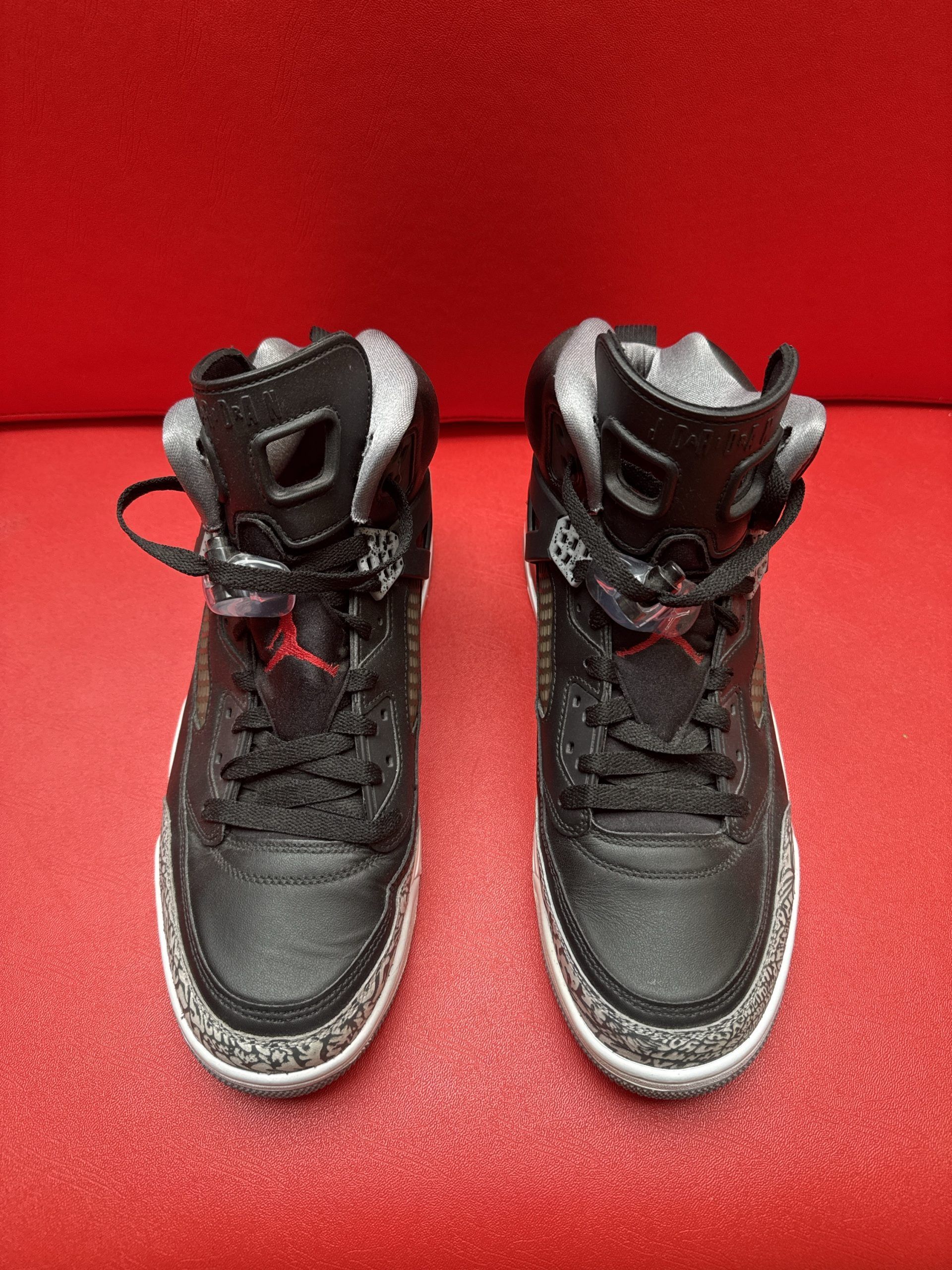 Black and gray Air Jordan sneakers on a red surface. One shoe is upside down, showing the sole.