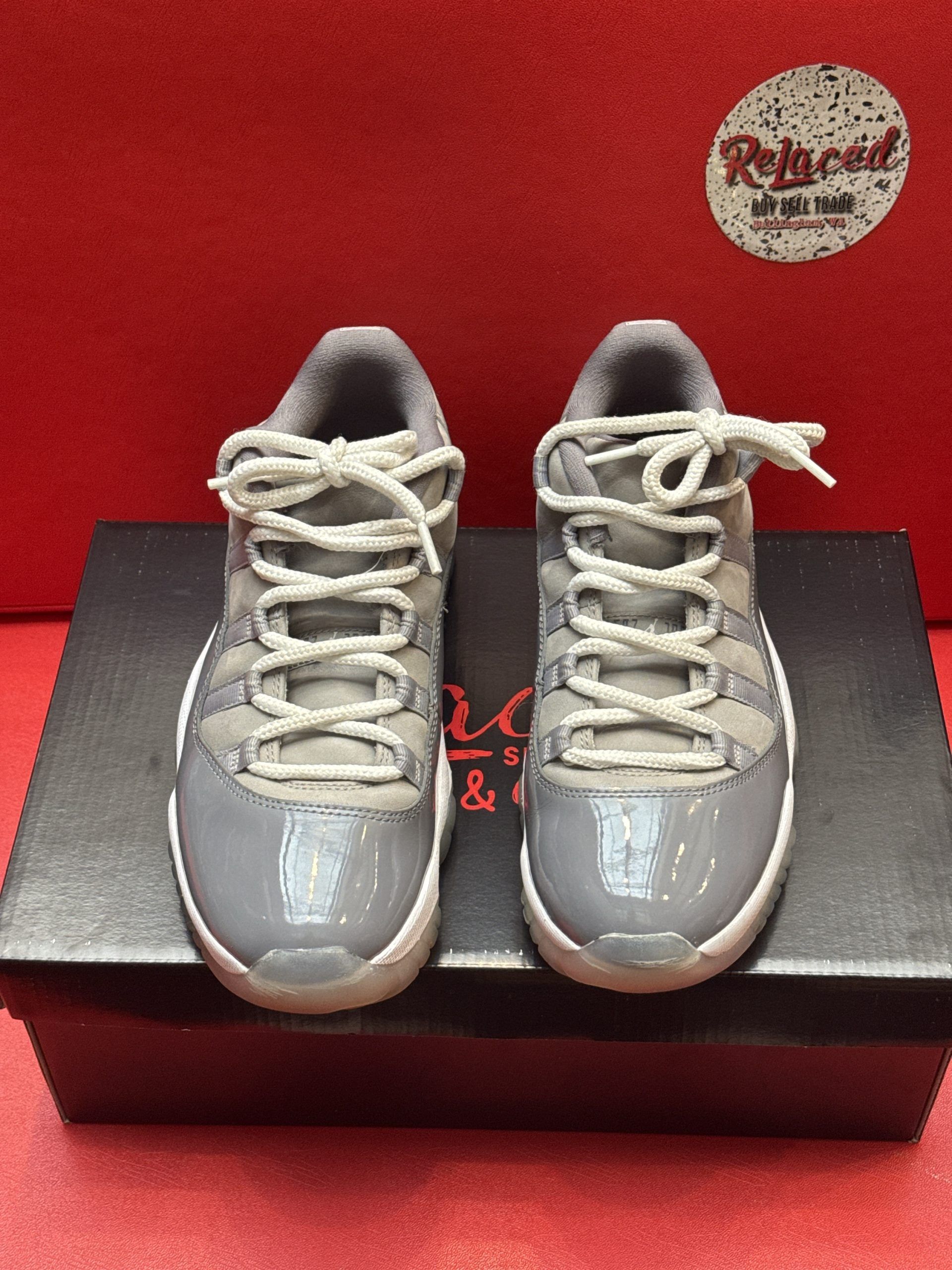 Gray Air Jordan 11 Retro low-top sneakers on a black box, with a red background.