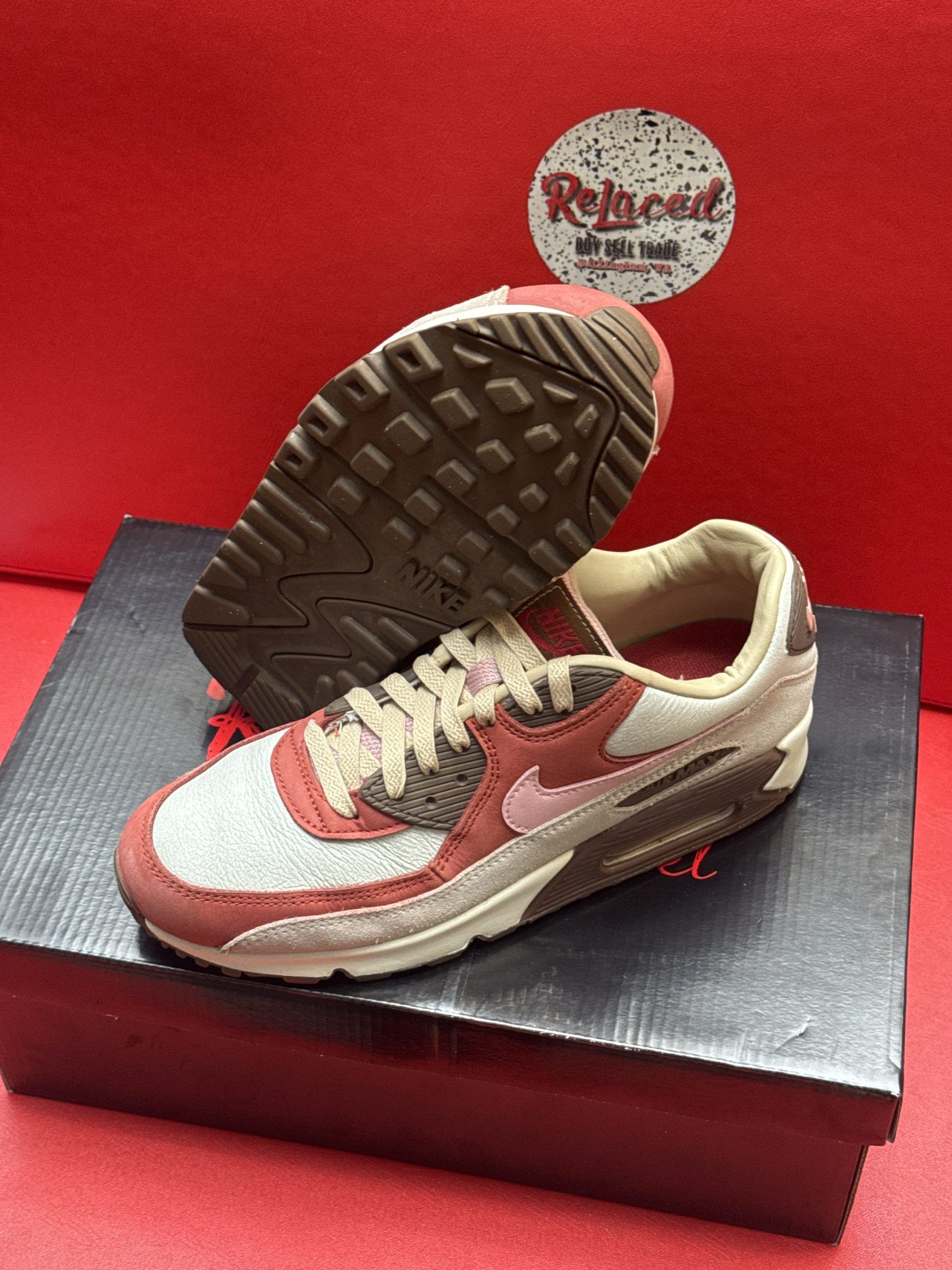 Nike Air Max 90 sneakers, red and tan colors, on a black shoebox with a red background.