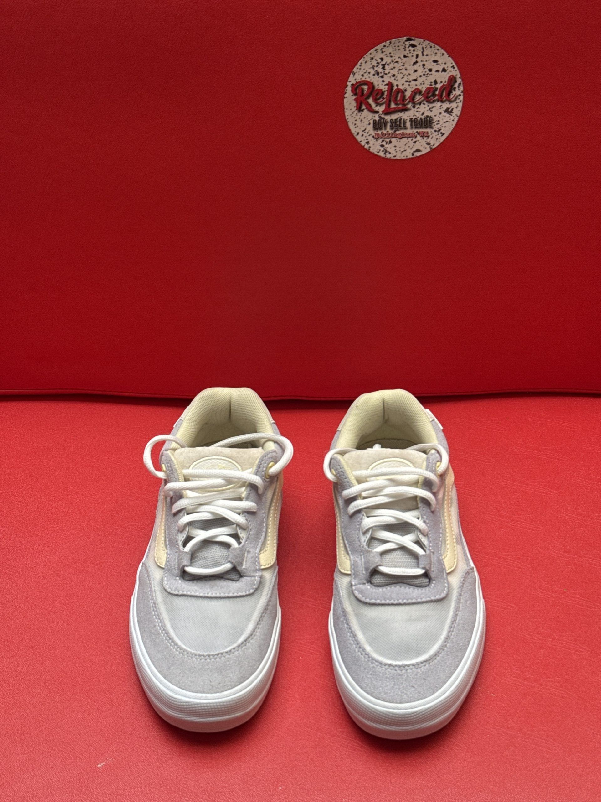 Gray and beige Vans sneaker, sole up. Red backdrop.