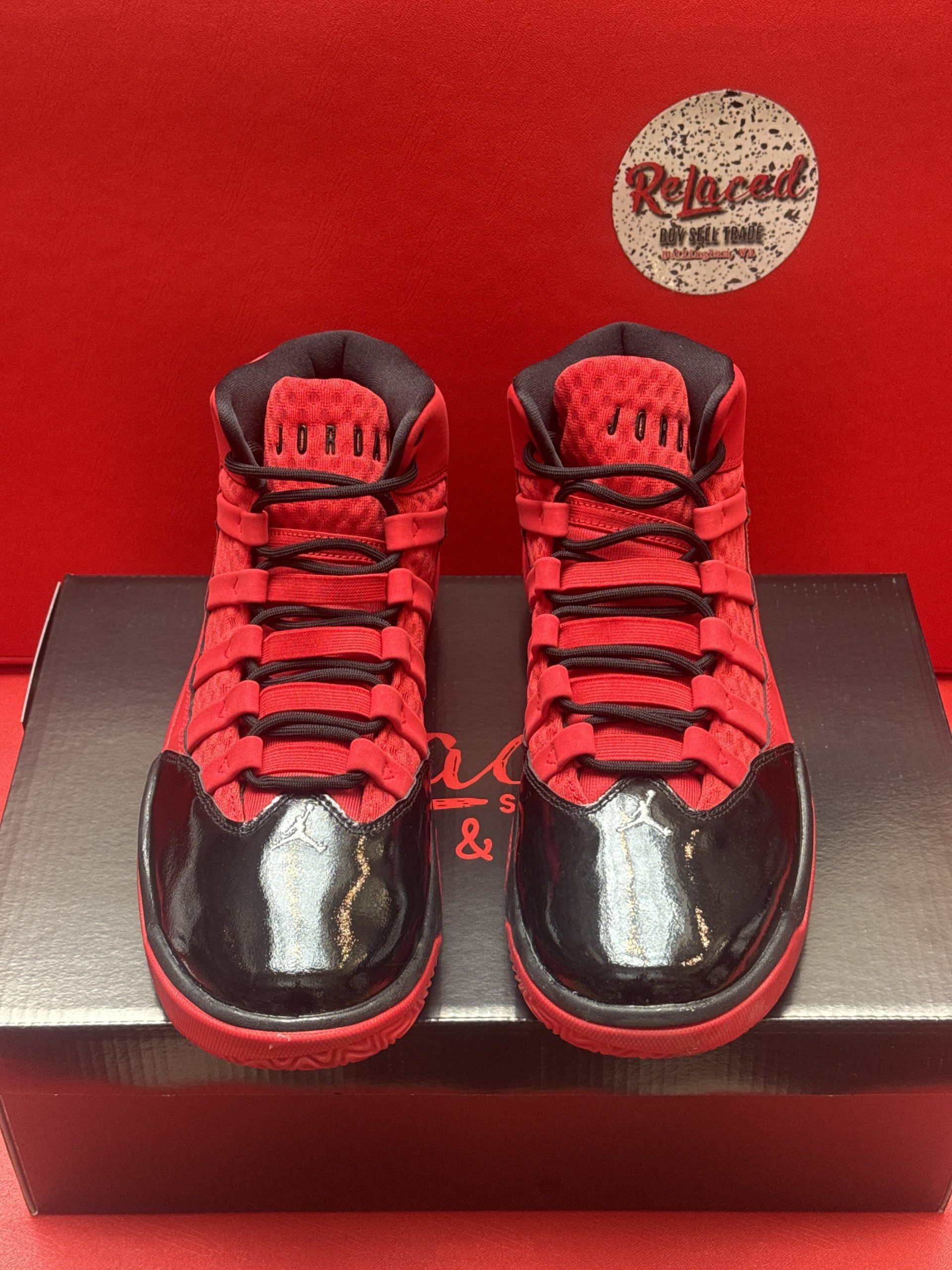Red and black toddler sneakers with black toe cap, sole up, on a box against a red backdrop.