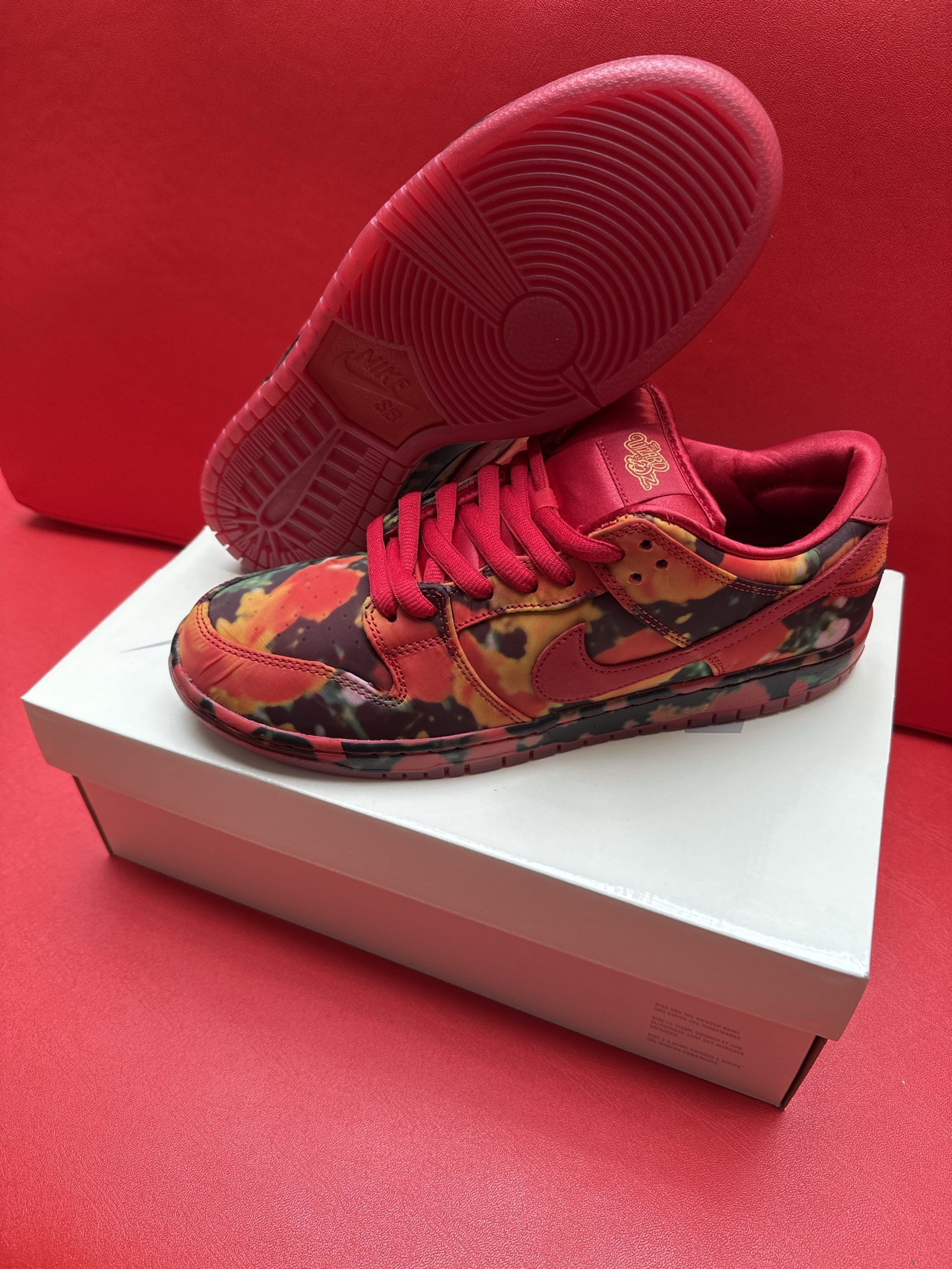 Red and orange patterned Nike Dunk Low sneaker on white box, red sole visible.