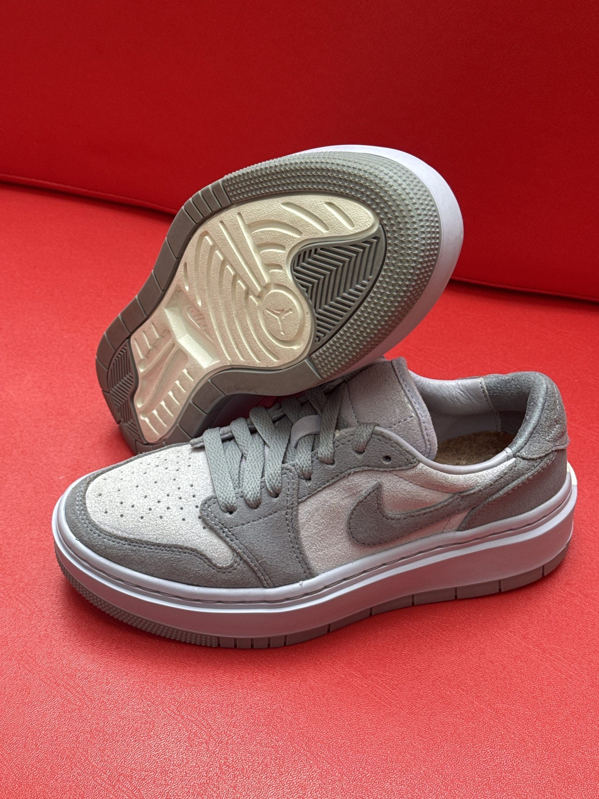 Gray and white Nike sneakers with visible sole, set against a red background.