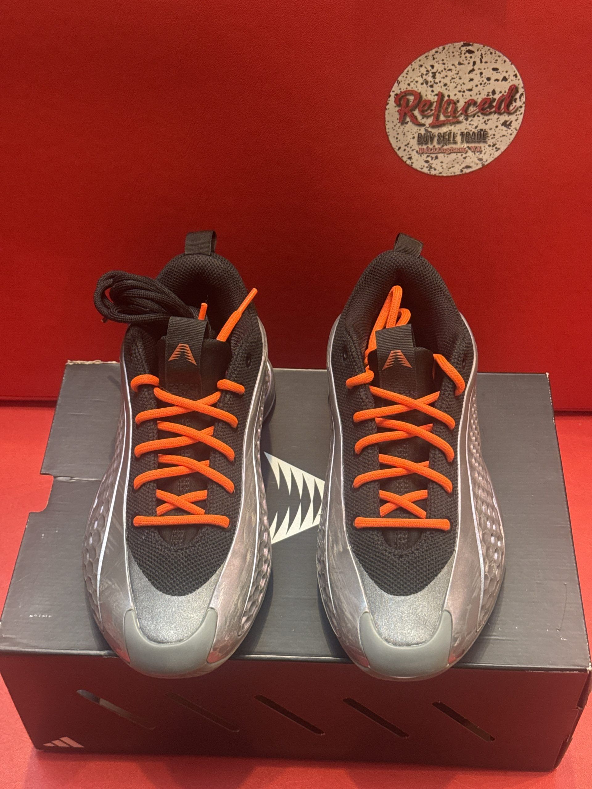 Black and orange sneakers sit on a dark box against a red background. One sneaker is flipped over.