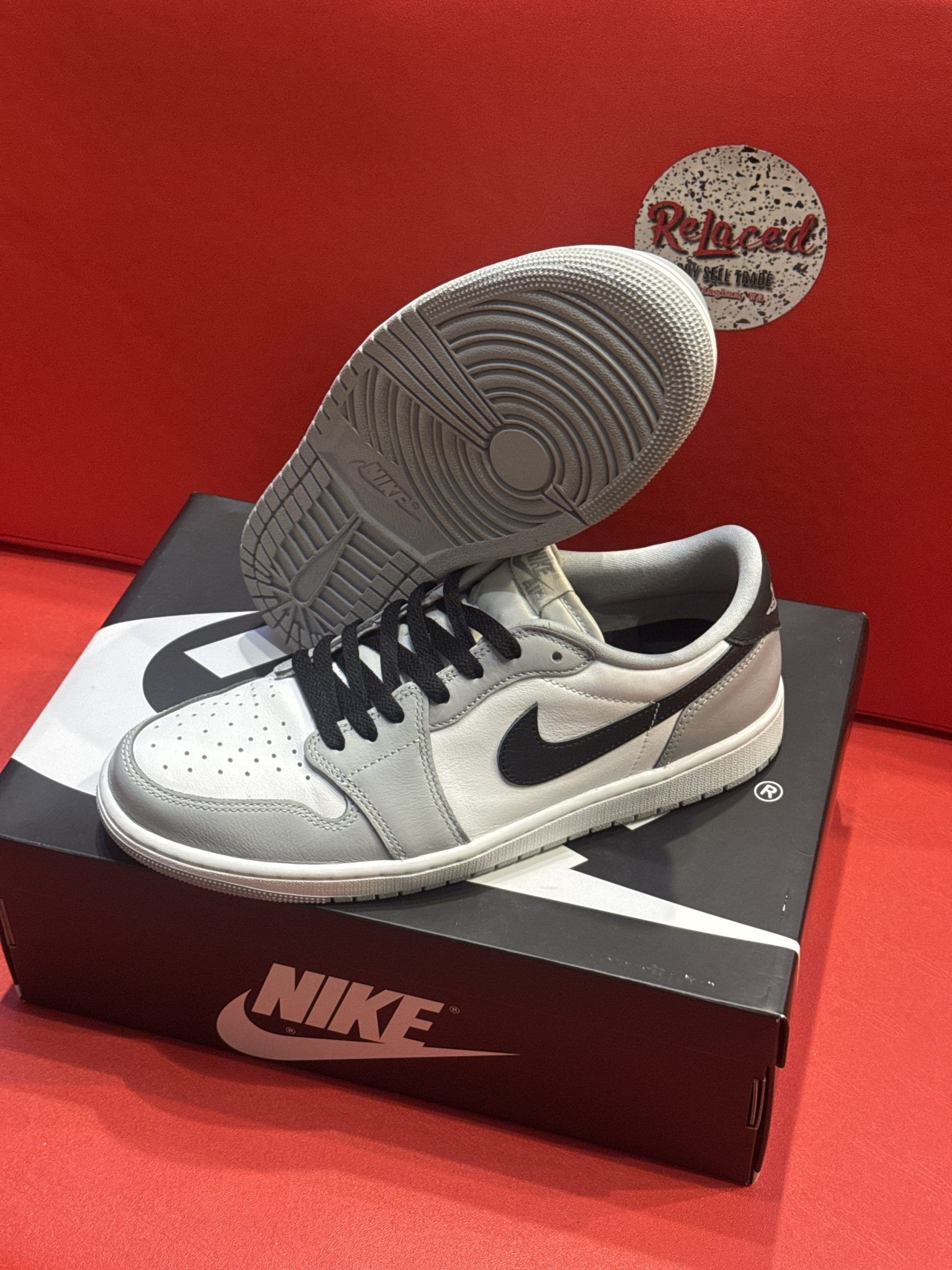 Air Jordan 1 Low sneakers, gray and white with a black Nike swoosh, on a black Nike shoe box.