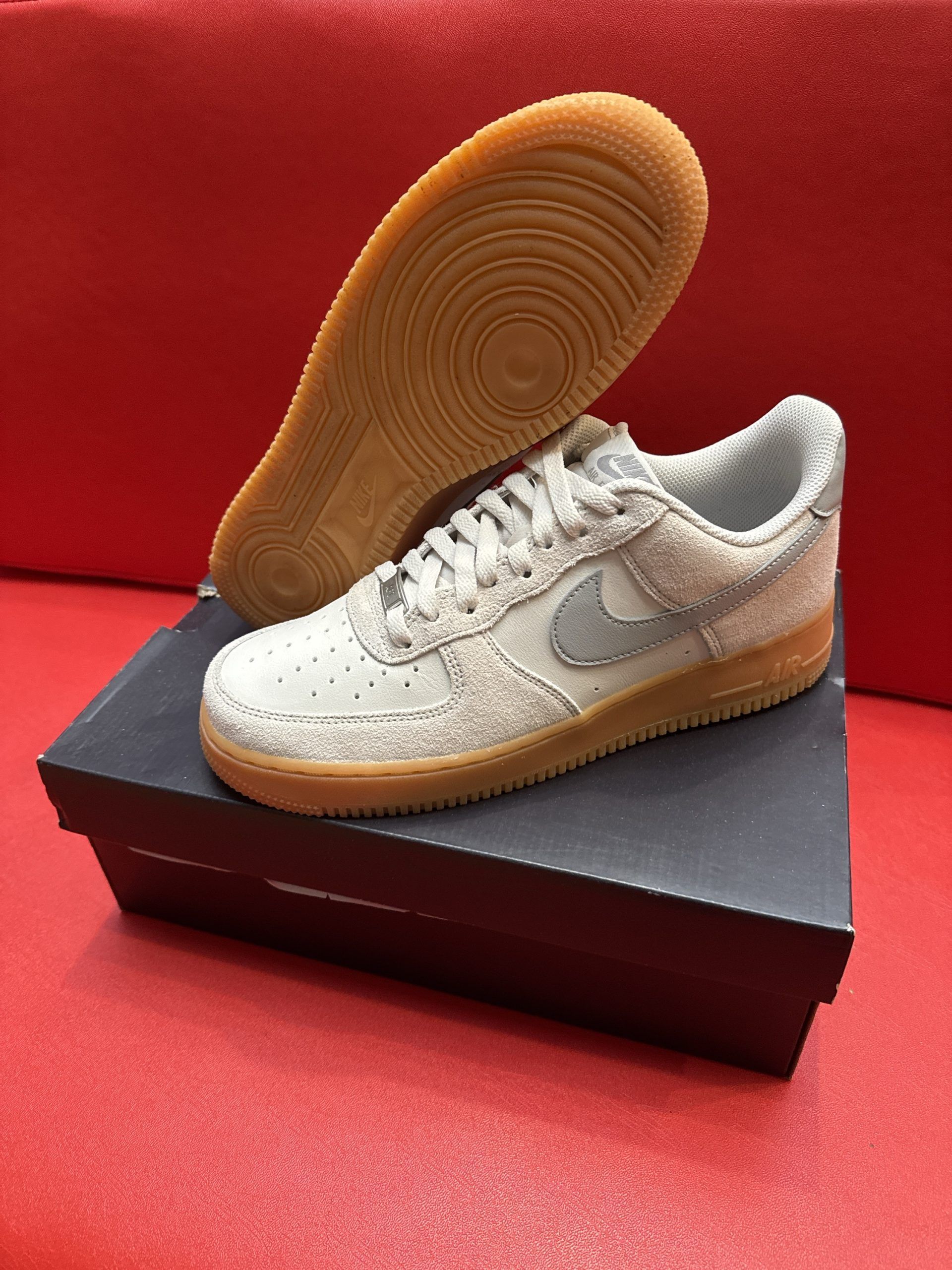 Gray Nike Air Force 1 sneakers with brown sole on a black box. The other shoe's sole is visible.