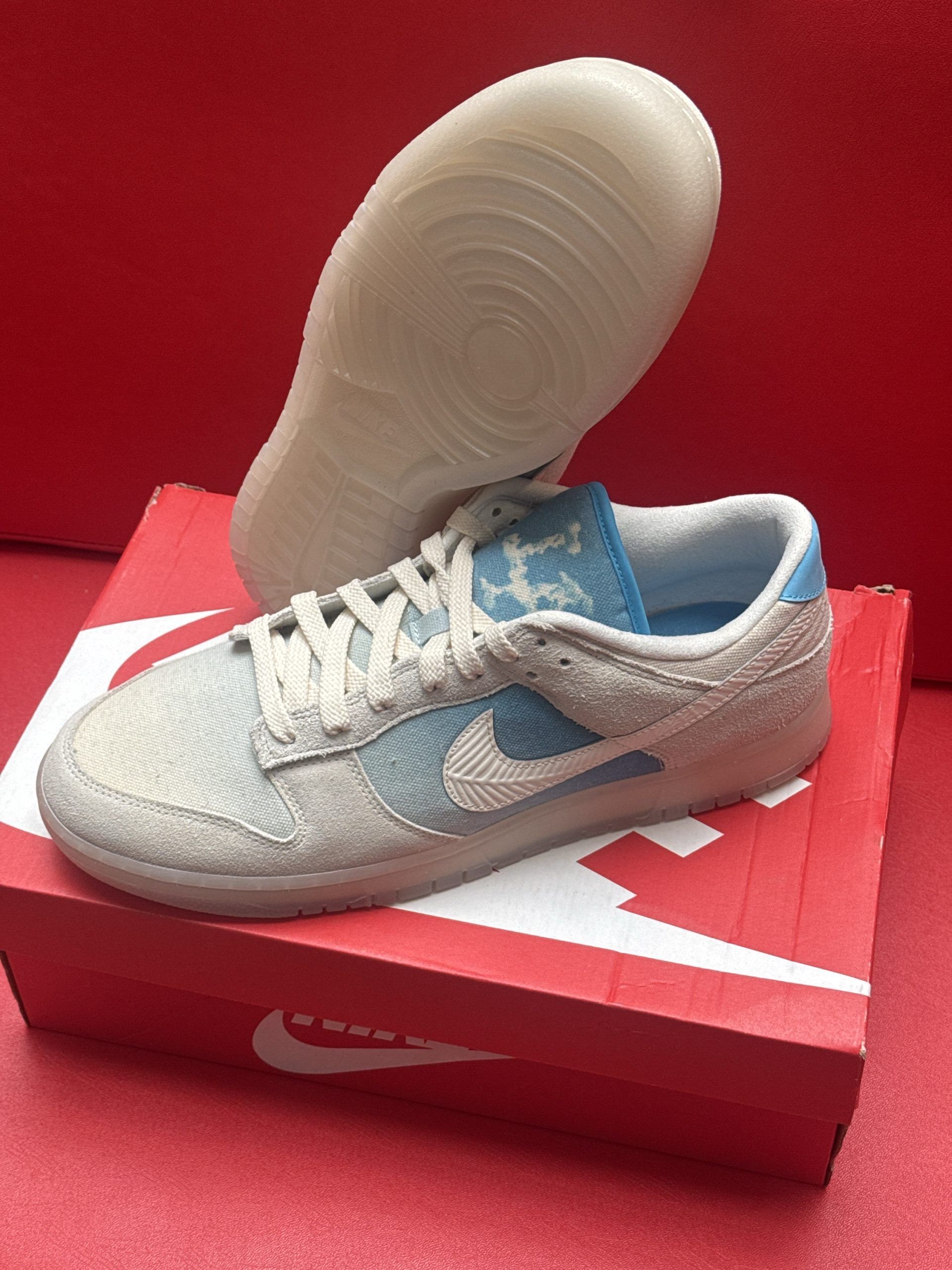Nike Dunk Low sneakers, light blue and cream colors, displayed on an orange Nike shoe box.