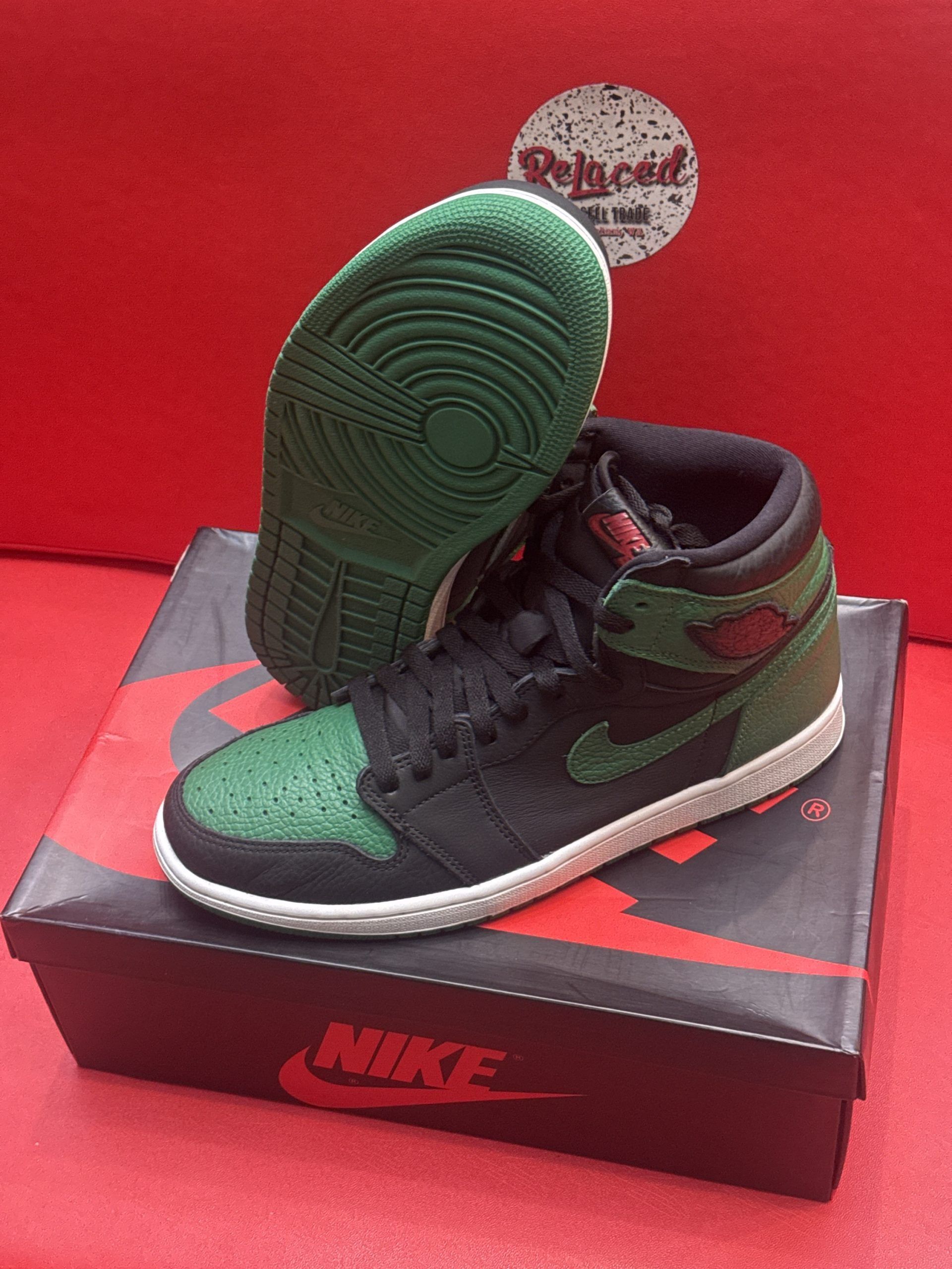 Green and black Air Jordan 1 sneakers on a box, red background.