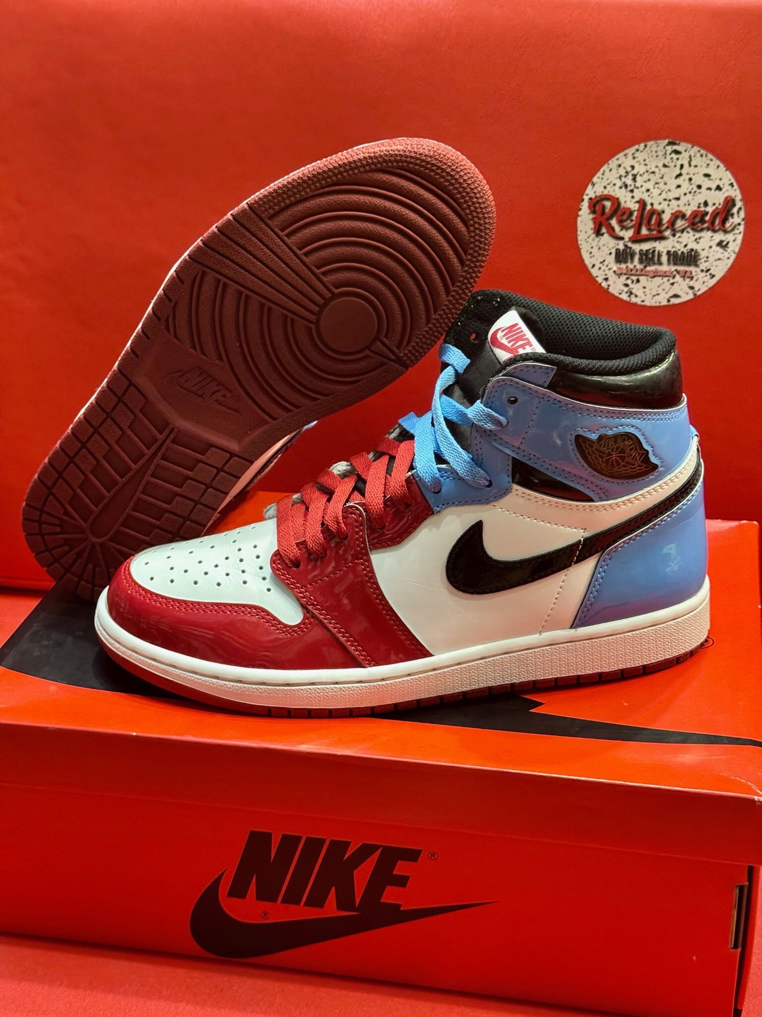 Air Jordan 1 sneaker with red, white, blue, and black accents, sitting on a red Nike box with a red sole visible.