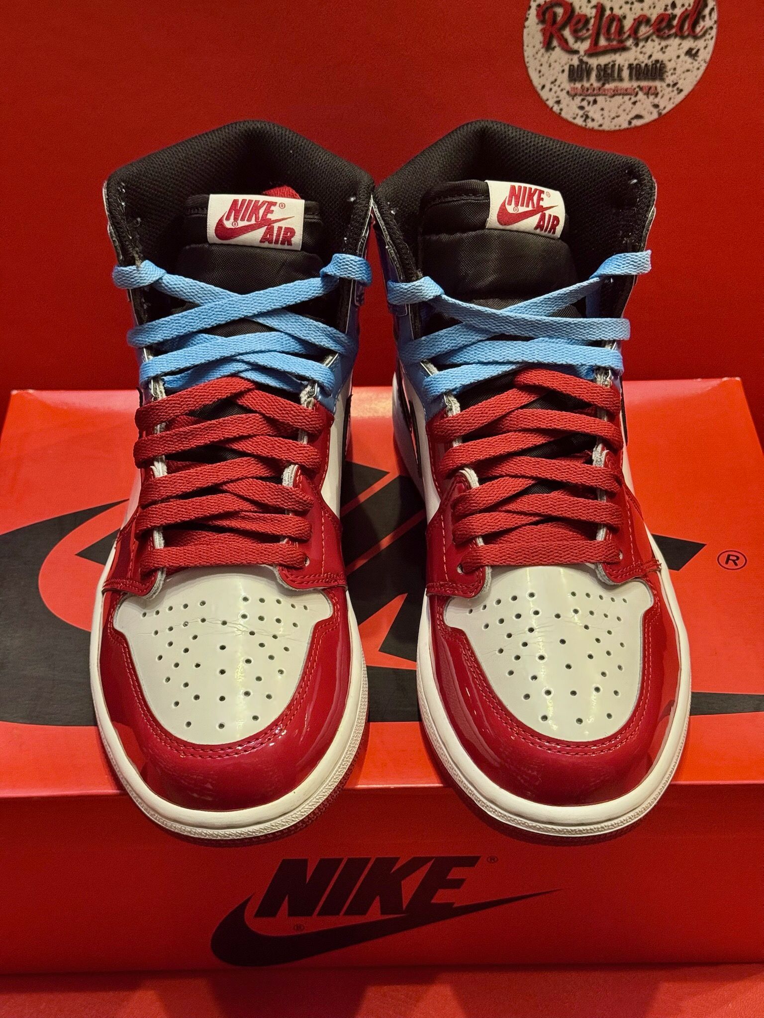 Air Jordan 1 sneaker with red, white, blue, and black accents, sitting on a red Nike box with a red sole visible.