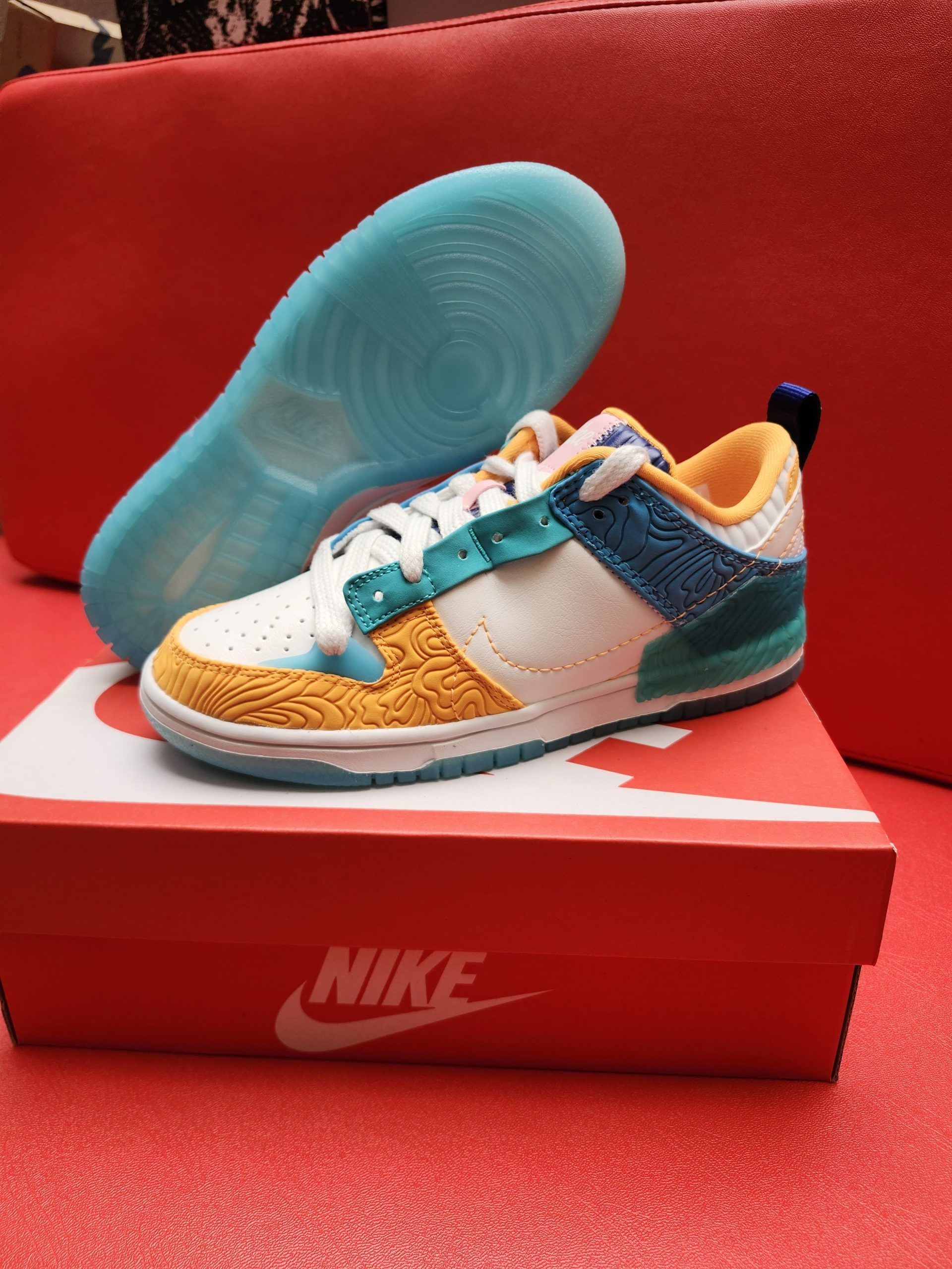 Colorful Nike Dunk low sneaker on an orange box, blue sole in background.