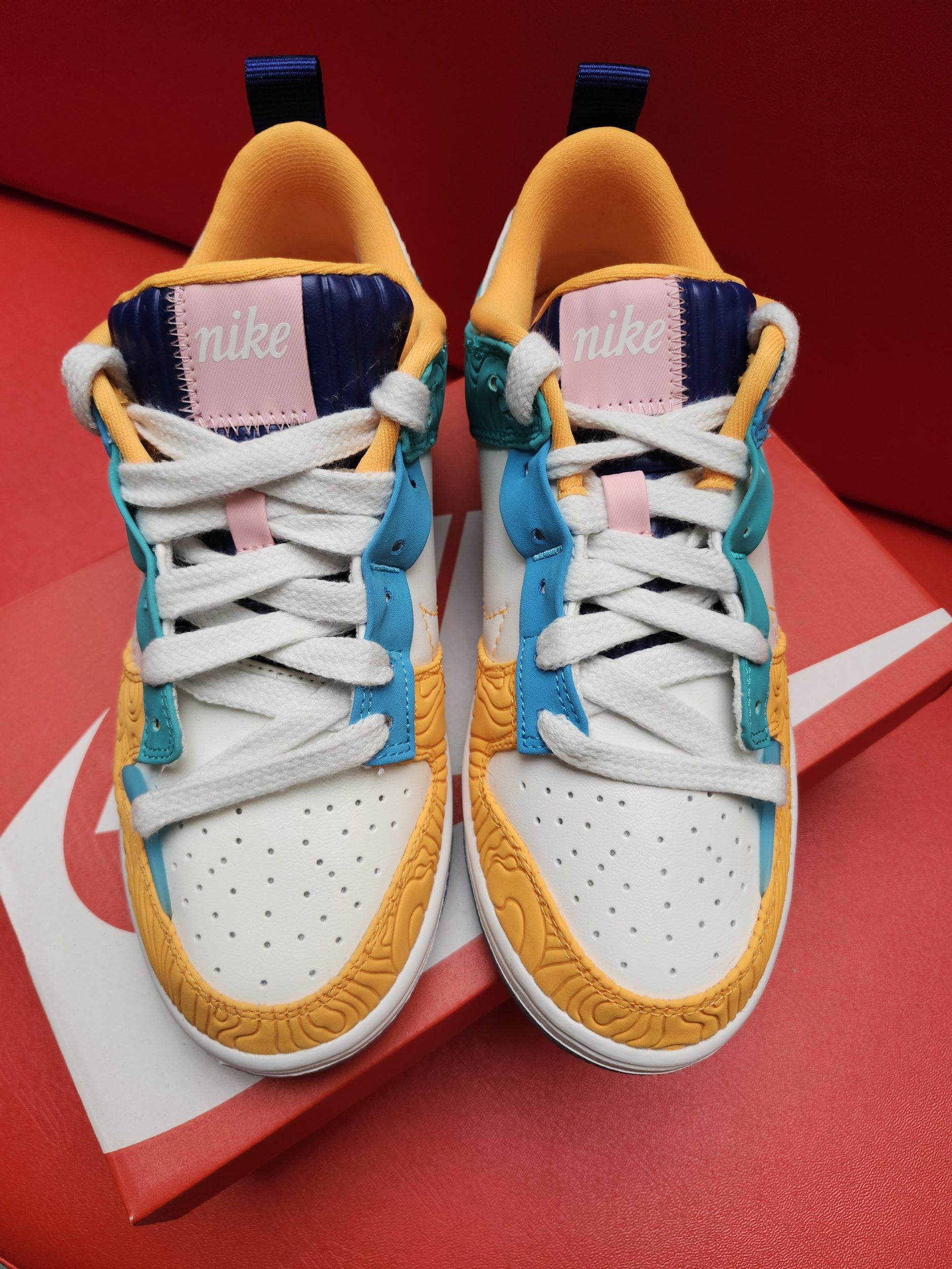 Colorful Nike Dunk low sneaker on an orange box, blue sole in background.