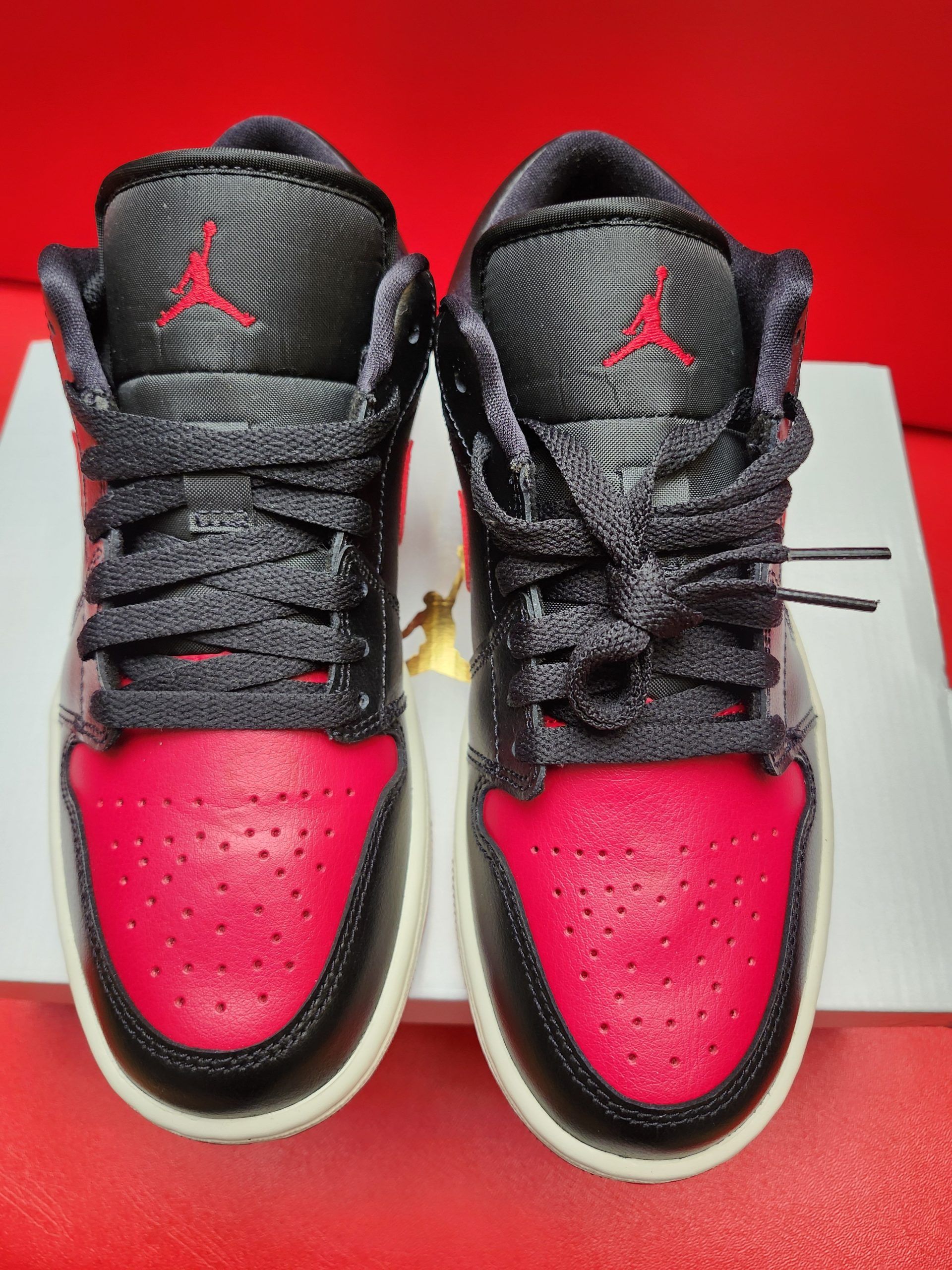 Black and red Air Jordan 1 Low sneaker with red sole and red swoosh, displayed on a white box.