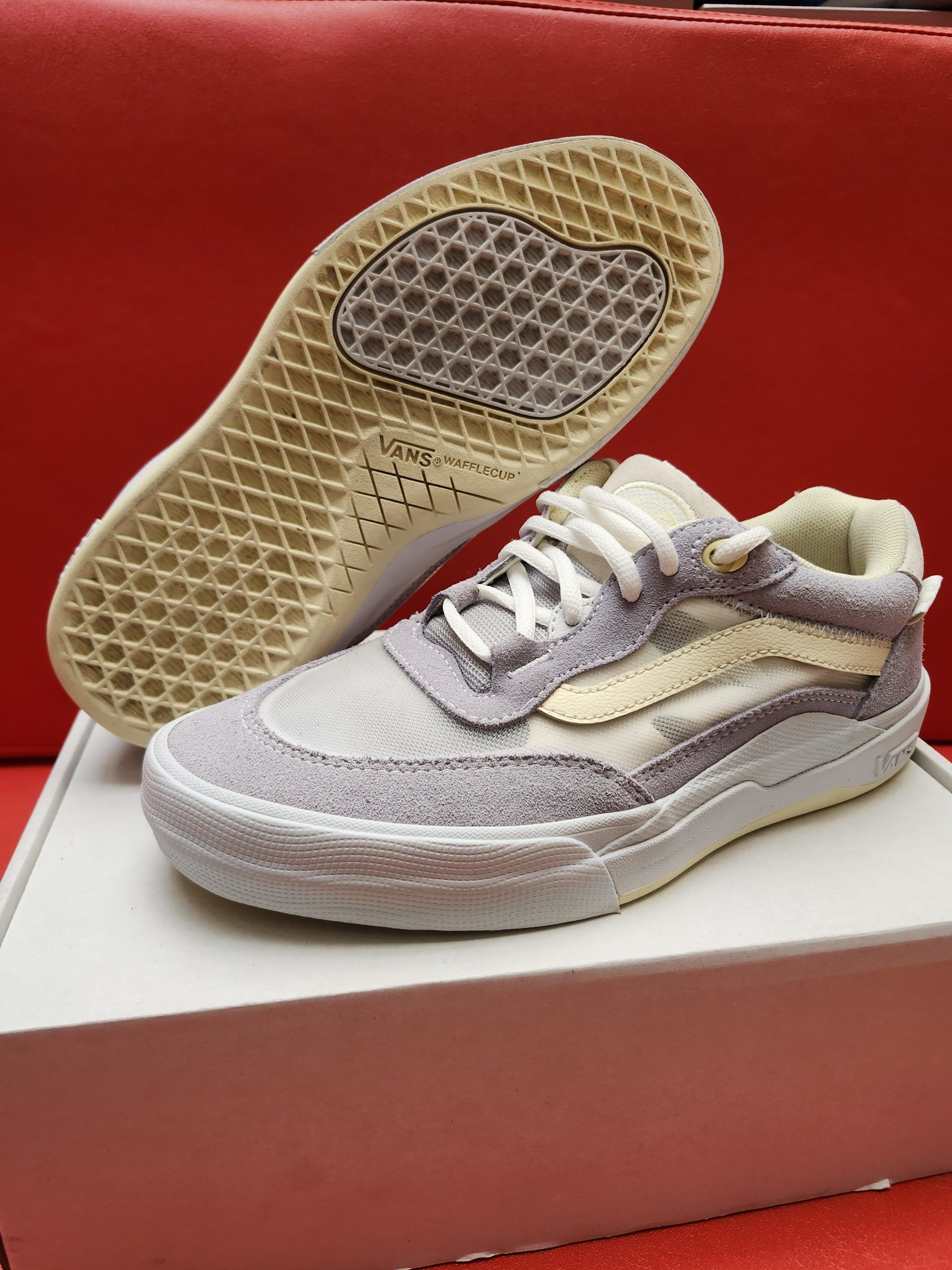Vans sneakers, purple and cream, on a white box. Sole visible, red background.