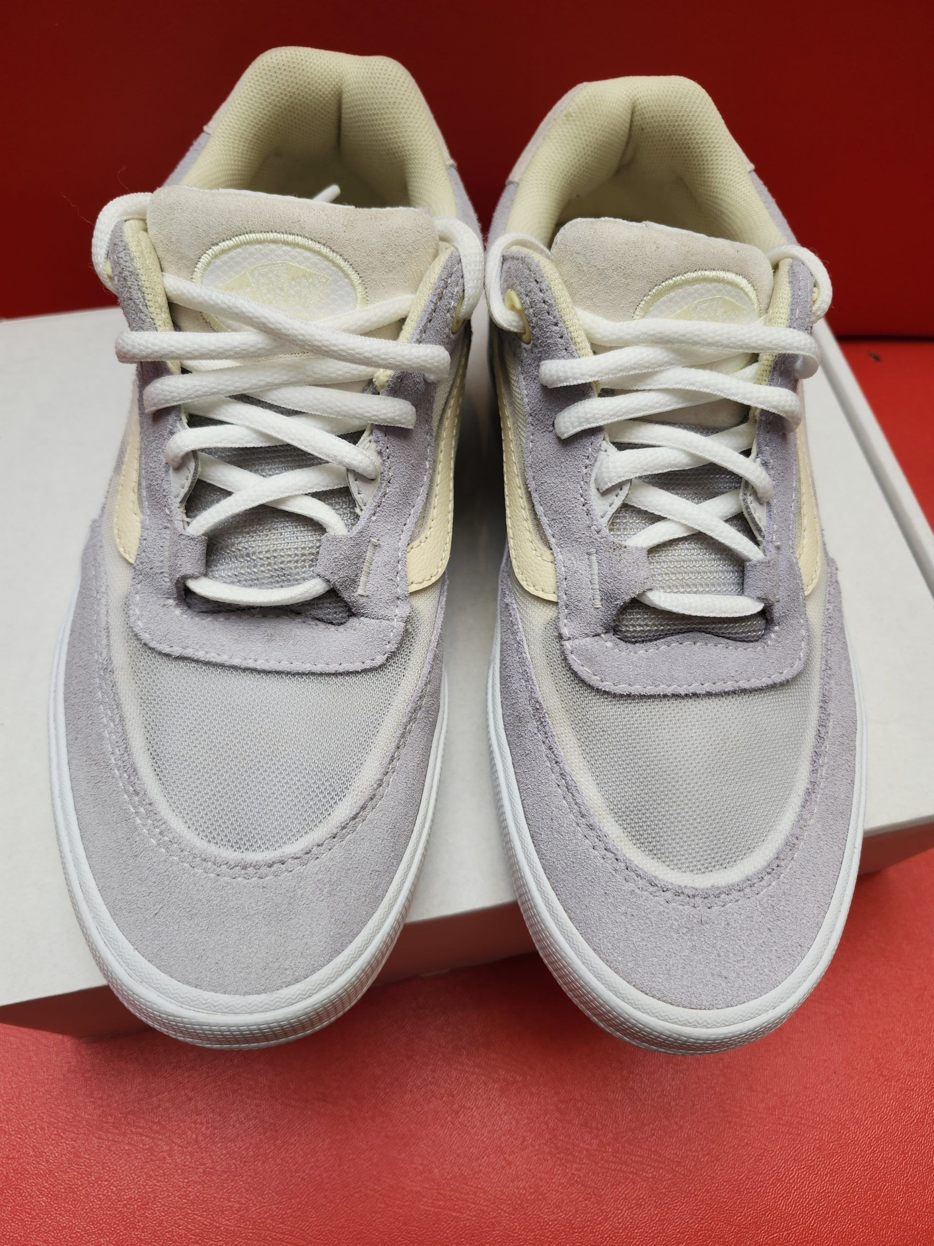 Vans sneakers, purple and cream, on a white box. Sole visible, red background.