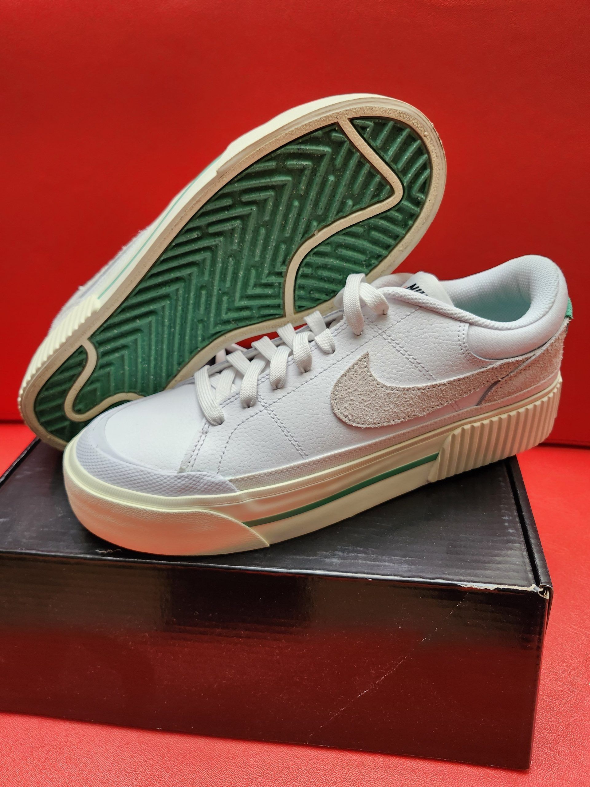 Light blue Nike sneakers on a black box, green and white sole, red background.
