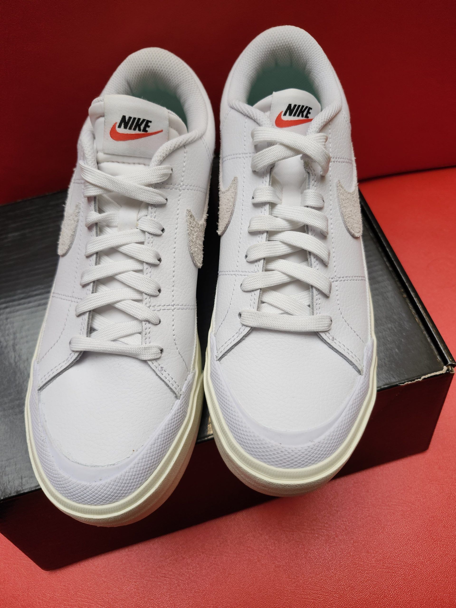 Light blue Nike sneakers on a black box, green and white sole, red background.