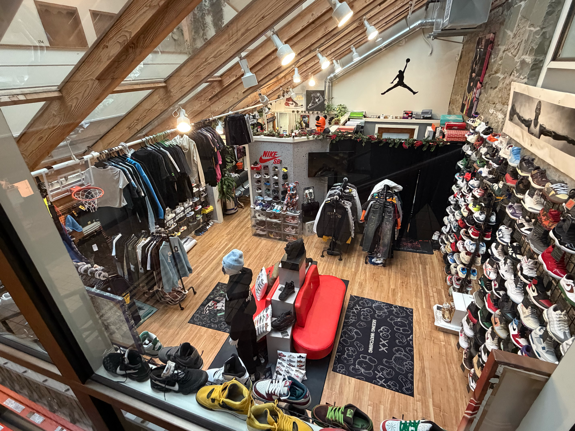 Relaced sneaker store interior with shoe displays on podiums, shelves, and a black curtain. Wooden floor and palm leaves.