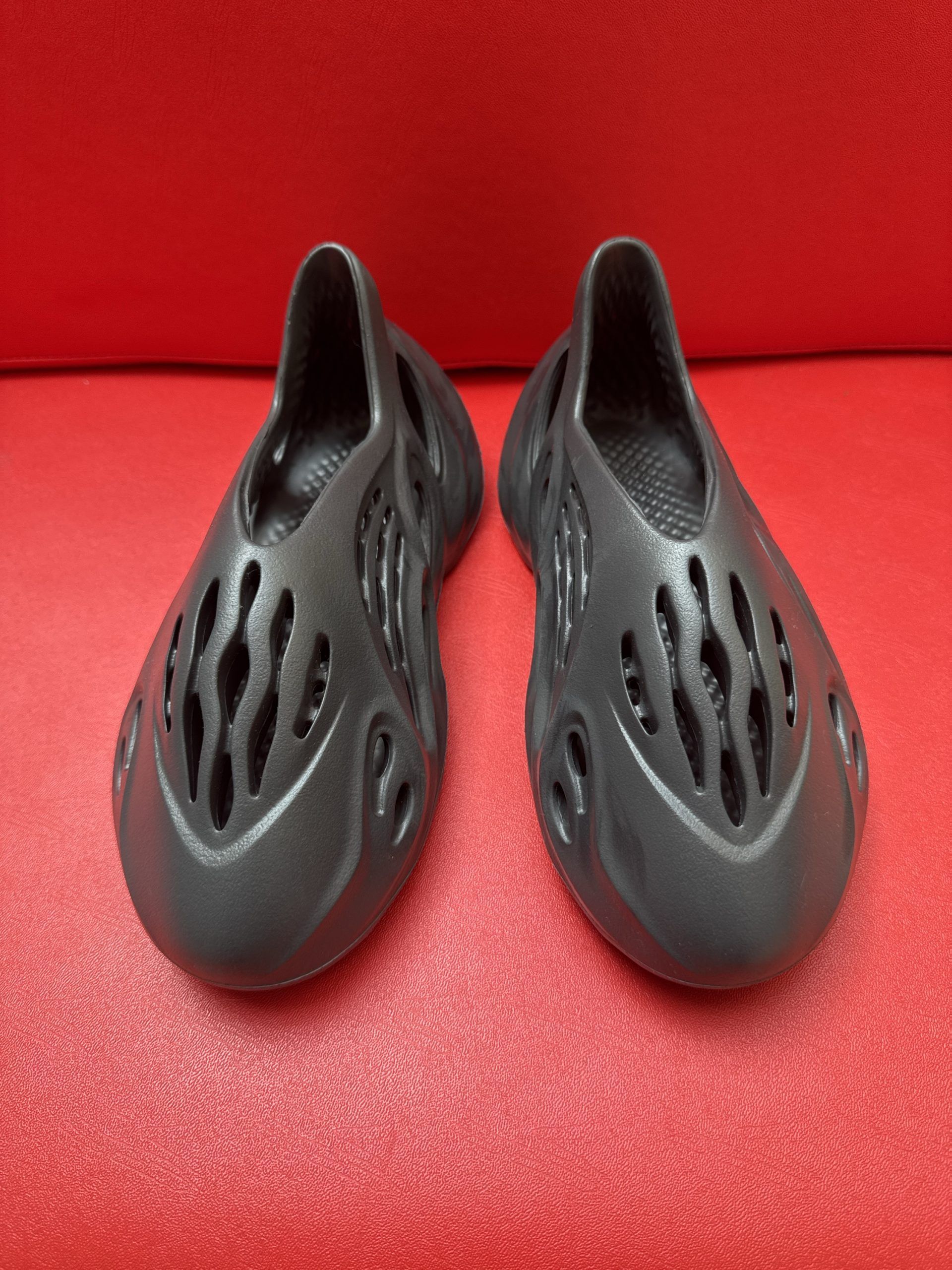 Black foam clog shoe on a red surface, with a heel portion flipped open.