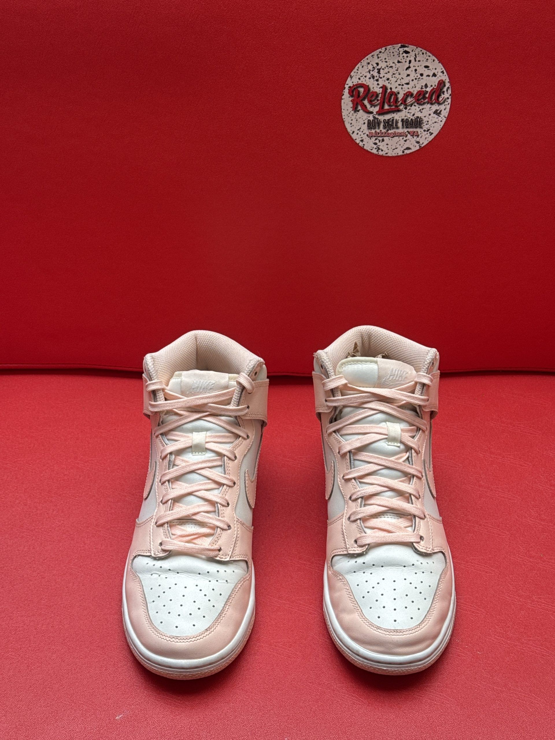 Pair of light pink Nike high-top sneakers with a white sole, set on a red surface.