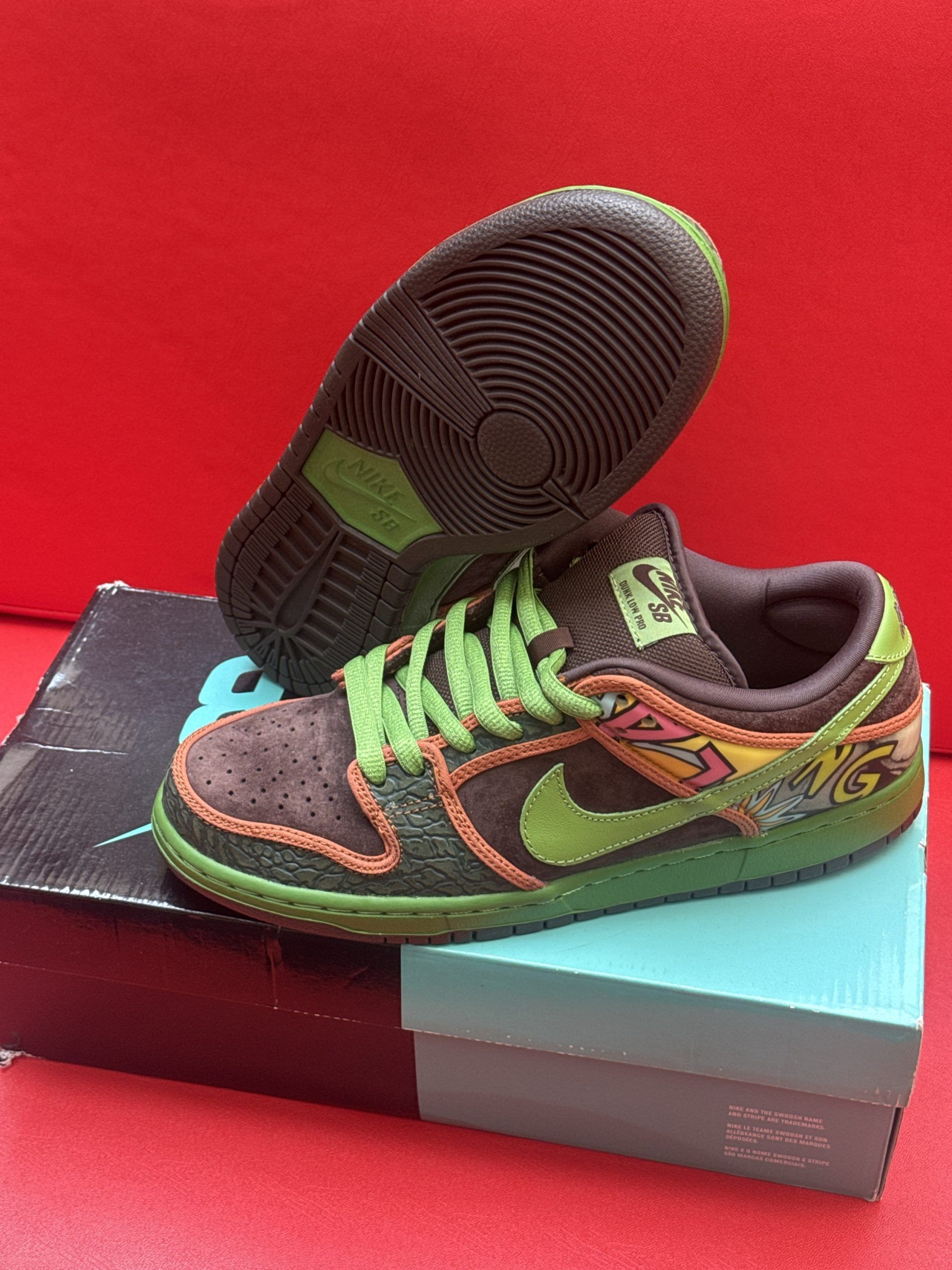 Brown Nike SB Dunk Low sneakers with green and orange accents, sitting on a box.