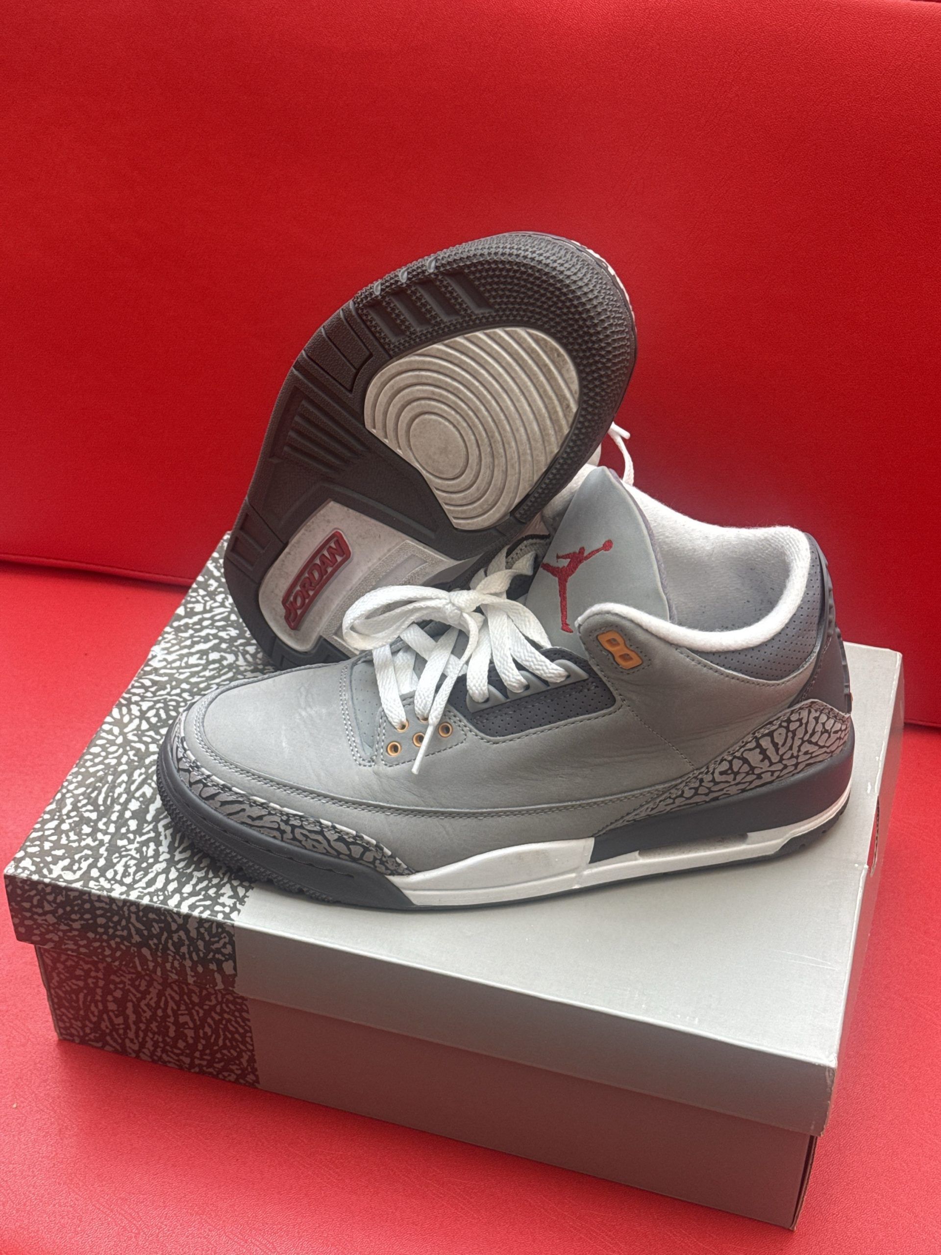 Gray Air Jordan 3 sneakers on a box, with one shoe turned over.