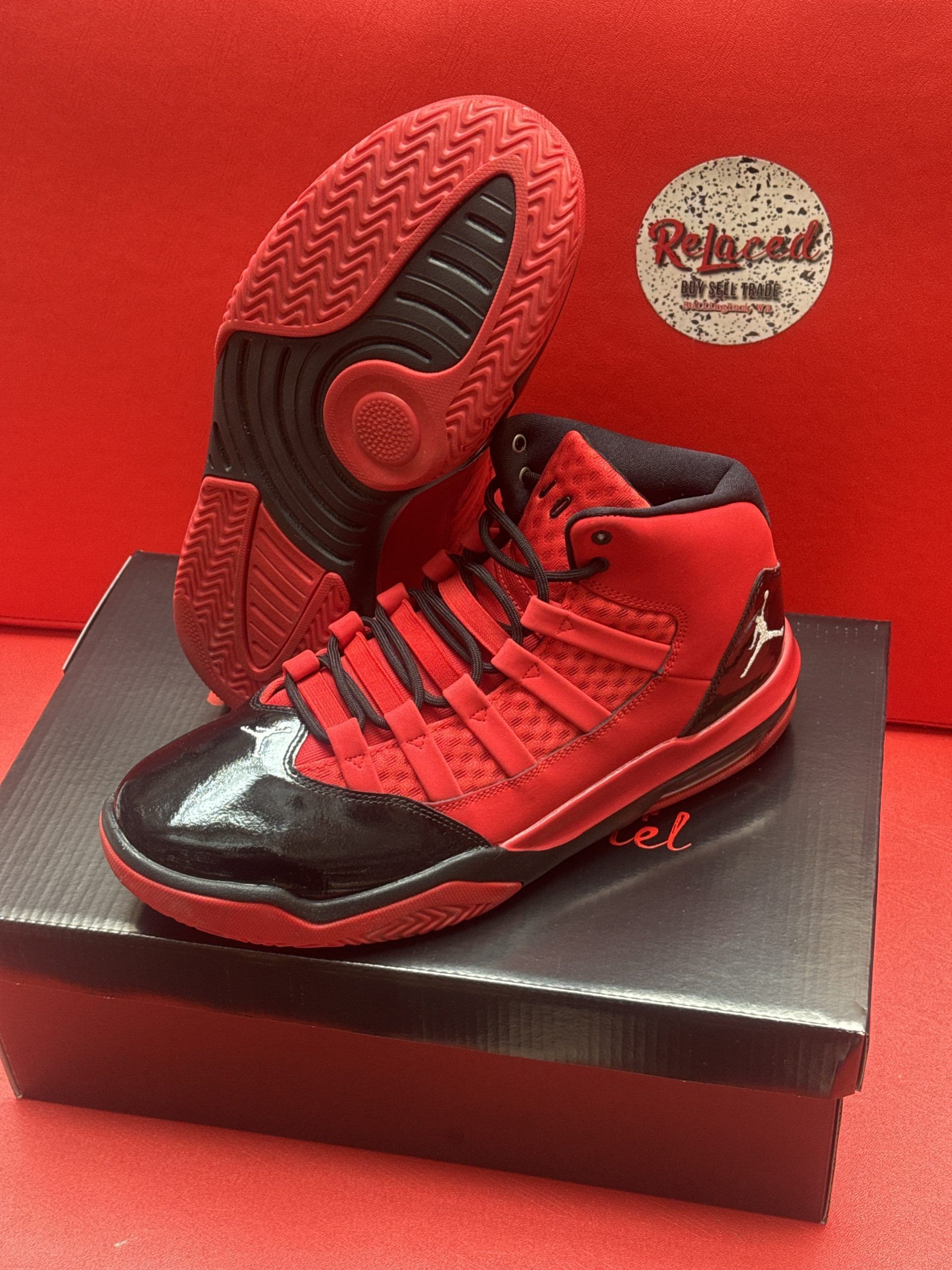 Red and black toddler sneakers with black toe cap, sole up, on a box against a red backdrop.