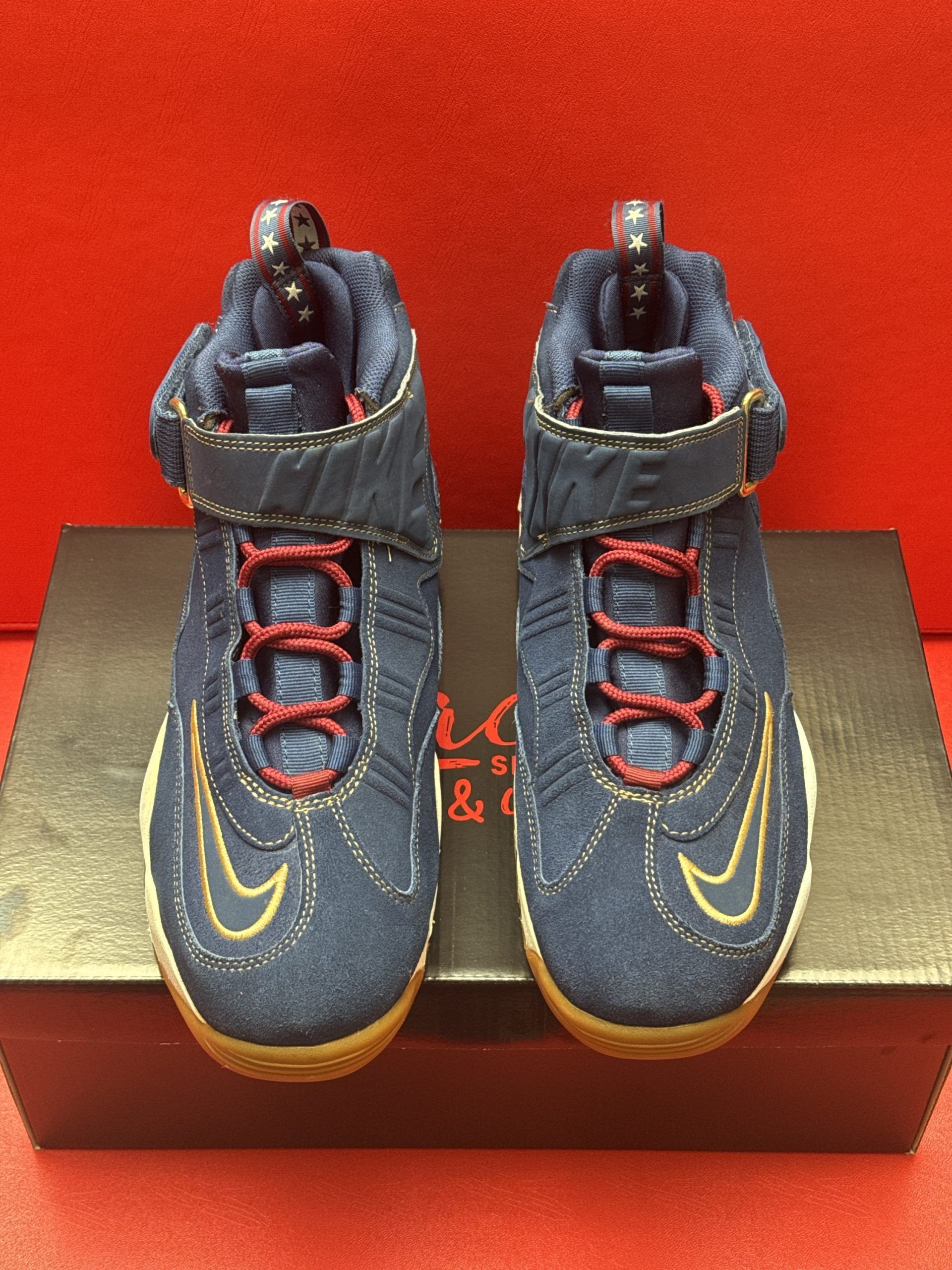 Blue and white Nike toddler sneakers with a gold swoosh and brown sole, resting on a box.