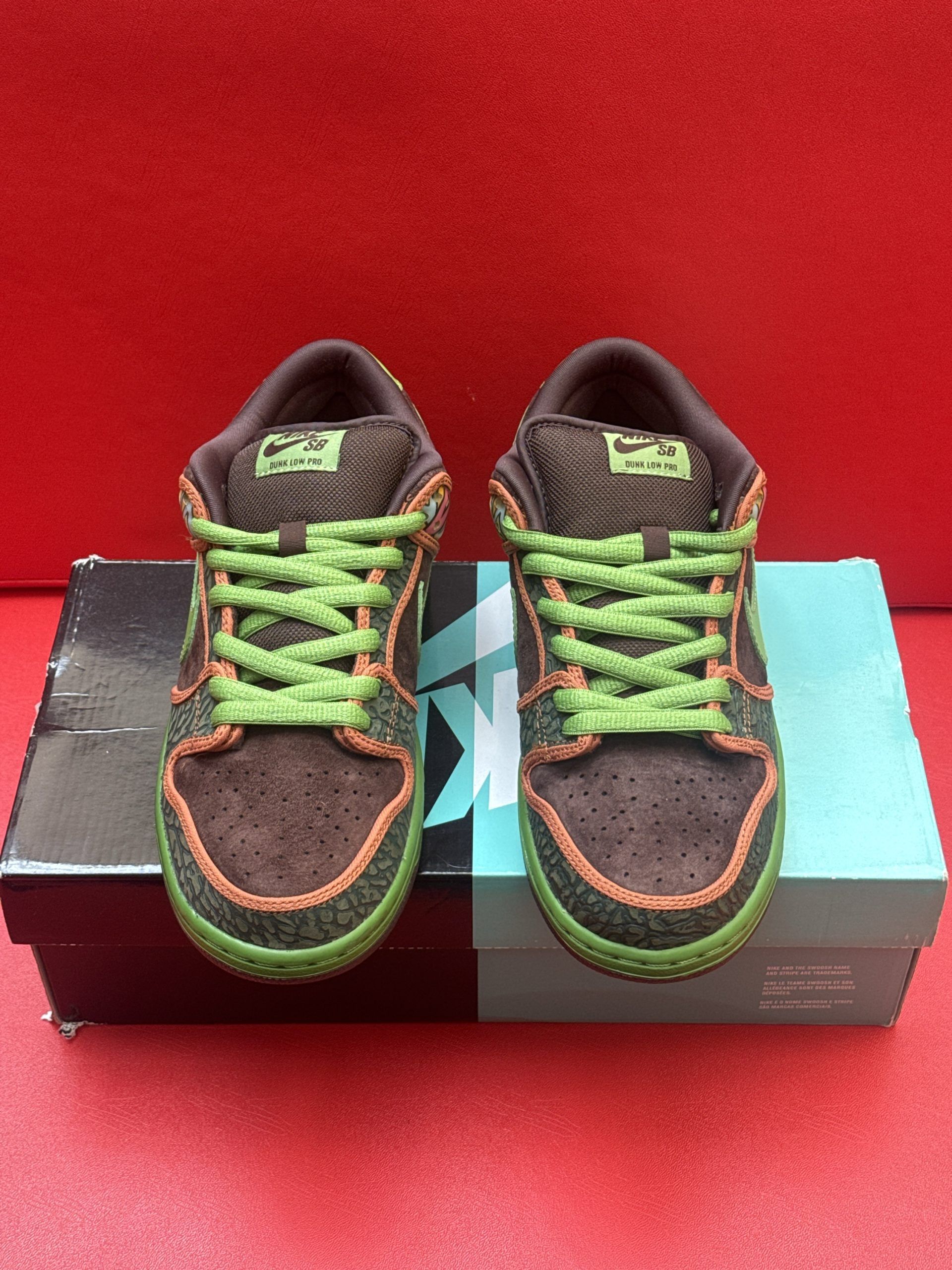 Brown Nike SB Dunk Low sneakers with green and orange accents, sitting on a box.