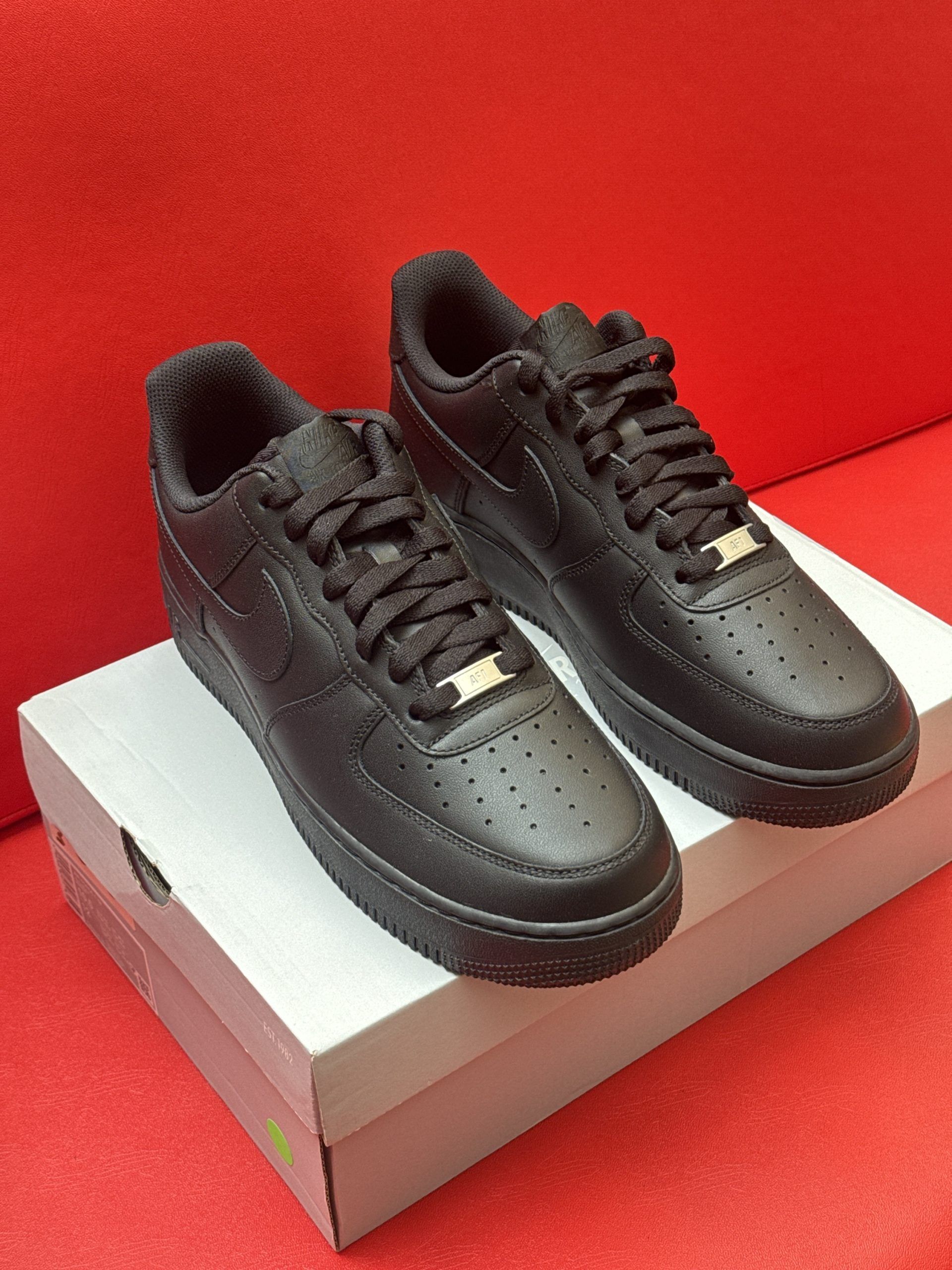 Black Nike Air Force 1 sneakers on a white shoebox against a red background.