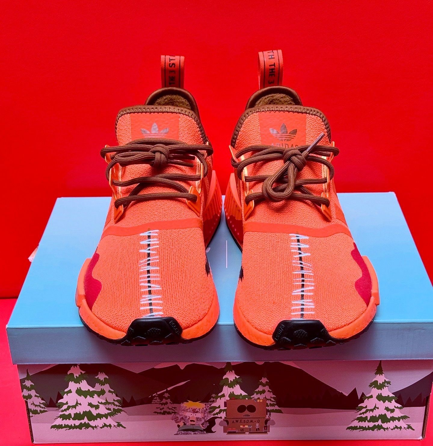 Orange Adidas NMD sneakers on a box with a South Park design; black sole visible.