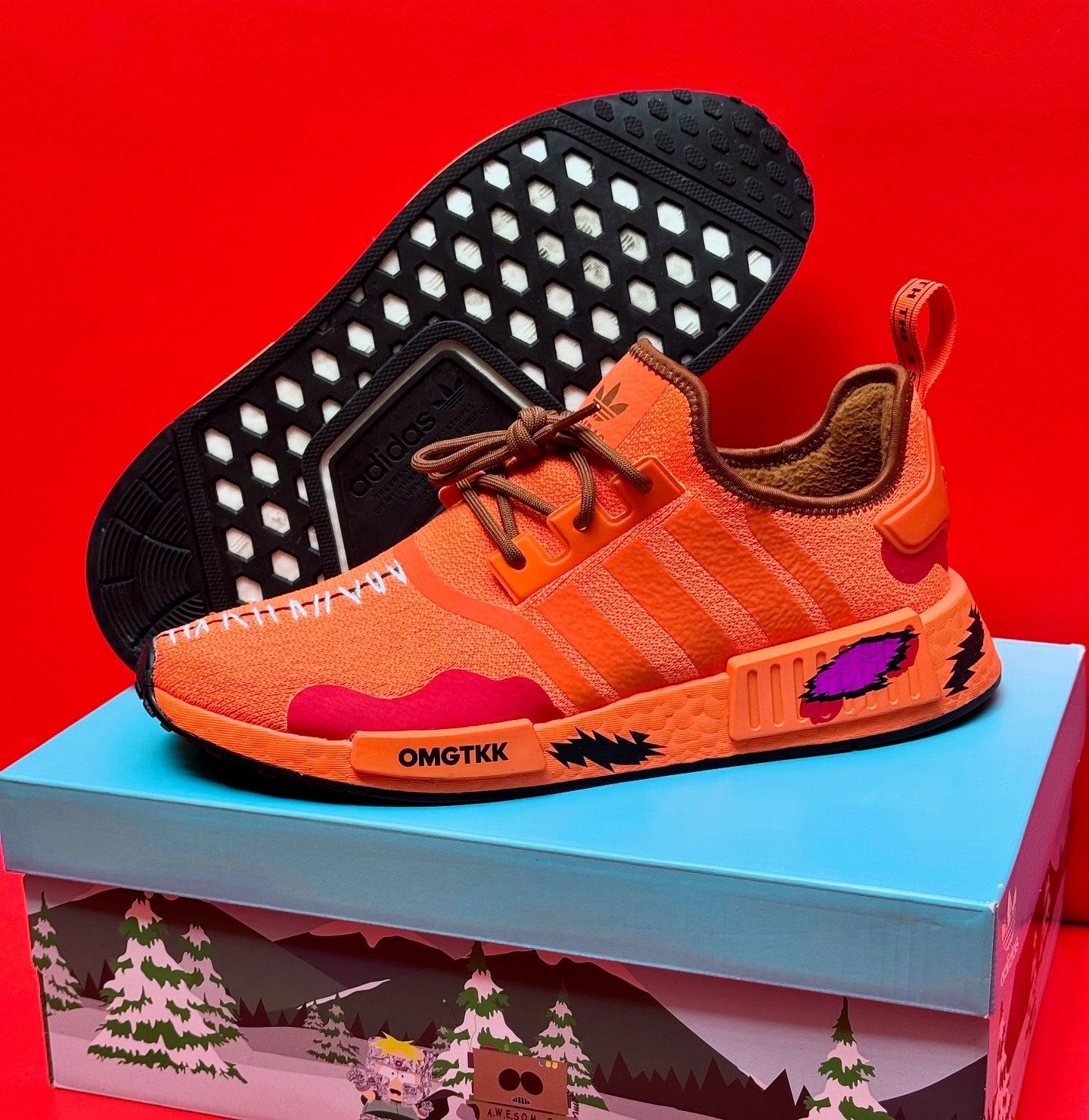 Orange Adidas NMD sneakers on a box with a South Park design; black sole visible.
