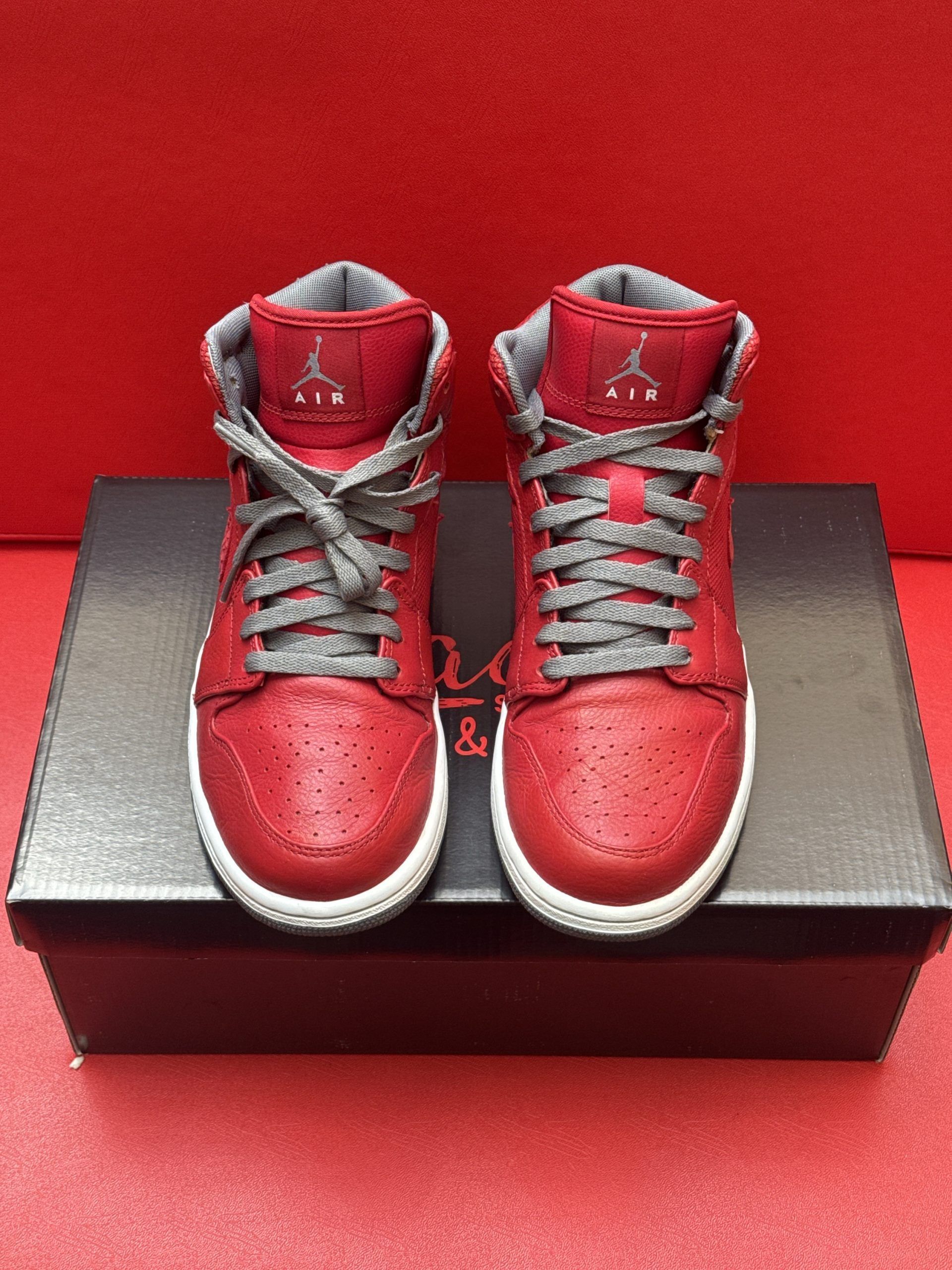 Red and white Air Jordan sneakers on a shoebox, with one sole facing upward against a red backdrop.