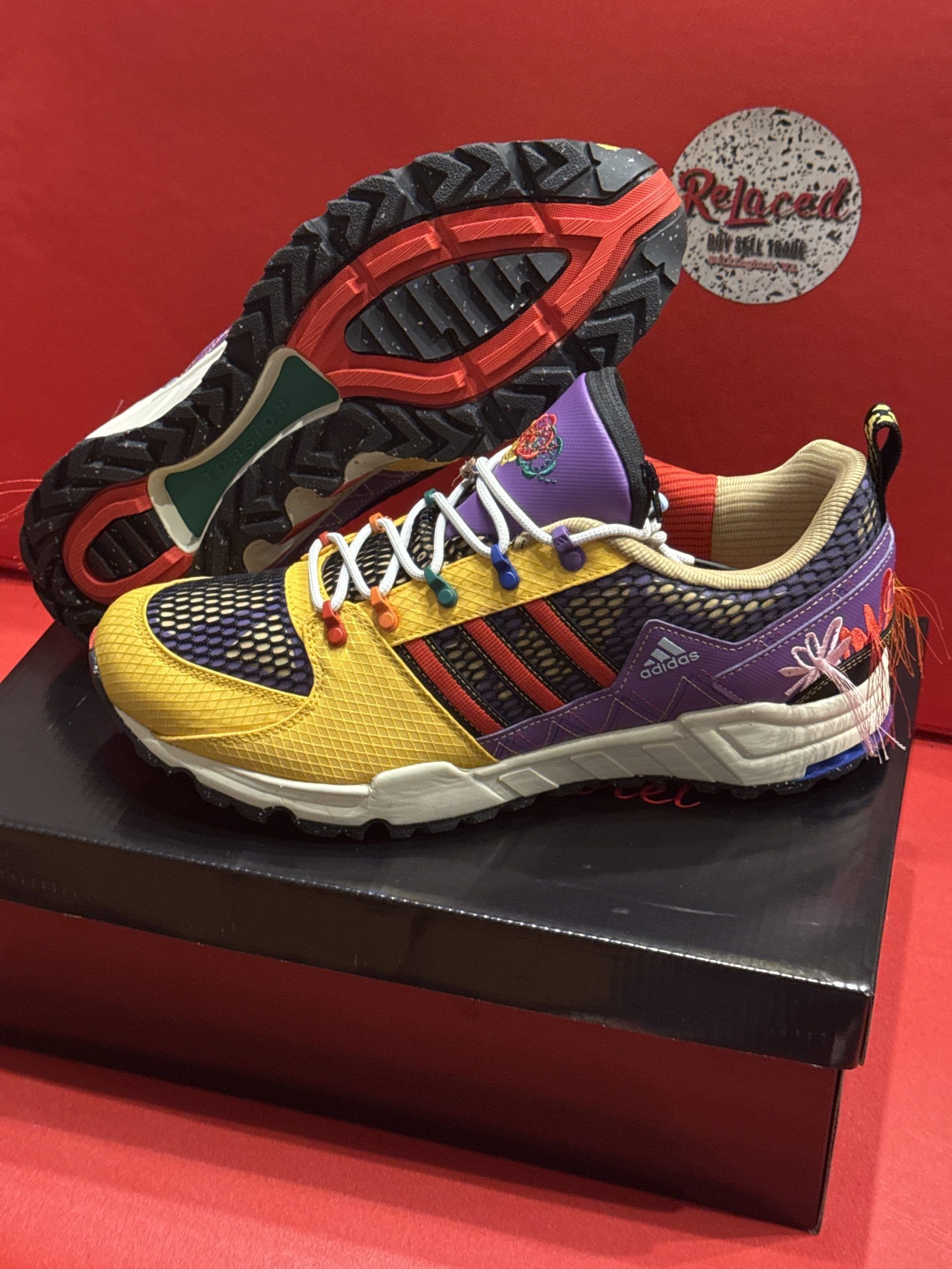 Adidas sneakers, yellow and purple, on a box, with a red background.