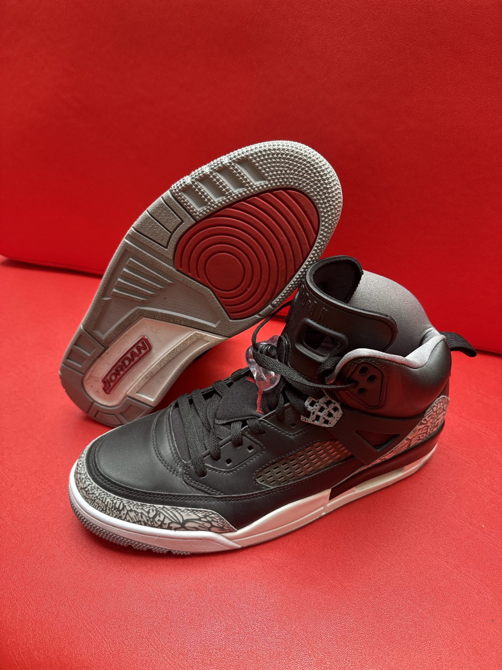 Black and gray Air Jordan sneakers on a red surface. One shoe is upside down, showing the sole.