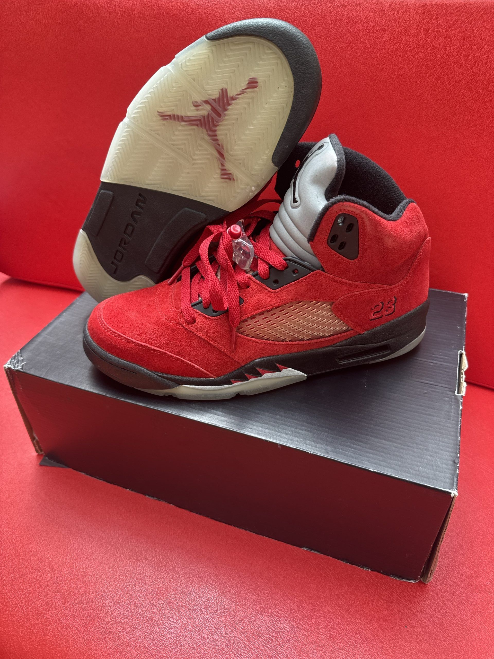 Red Air Jordan 5 sneakers, partially on a black shoebox, with a visible Jumpman logo on the sole.