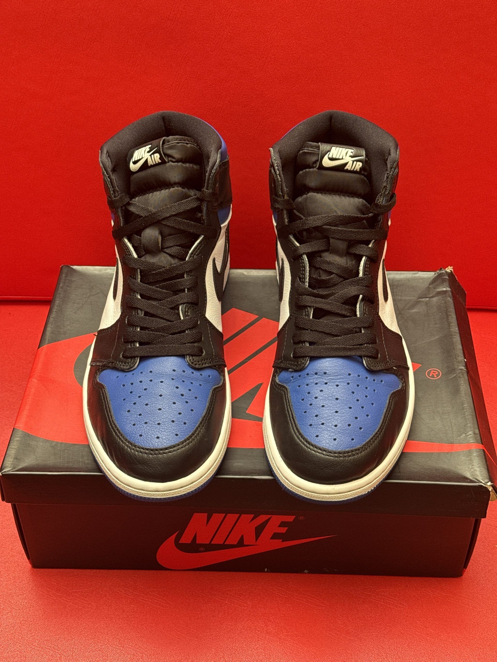 Pair of blue, black, and white Air Jordan 1 sneakers on a box with a red Nike logo; one shoe's sole is visible.