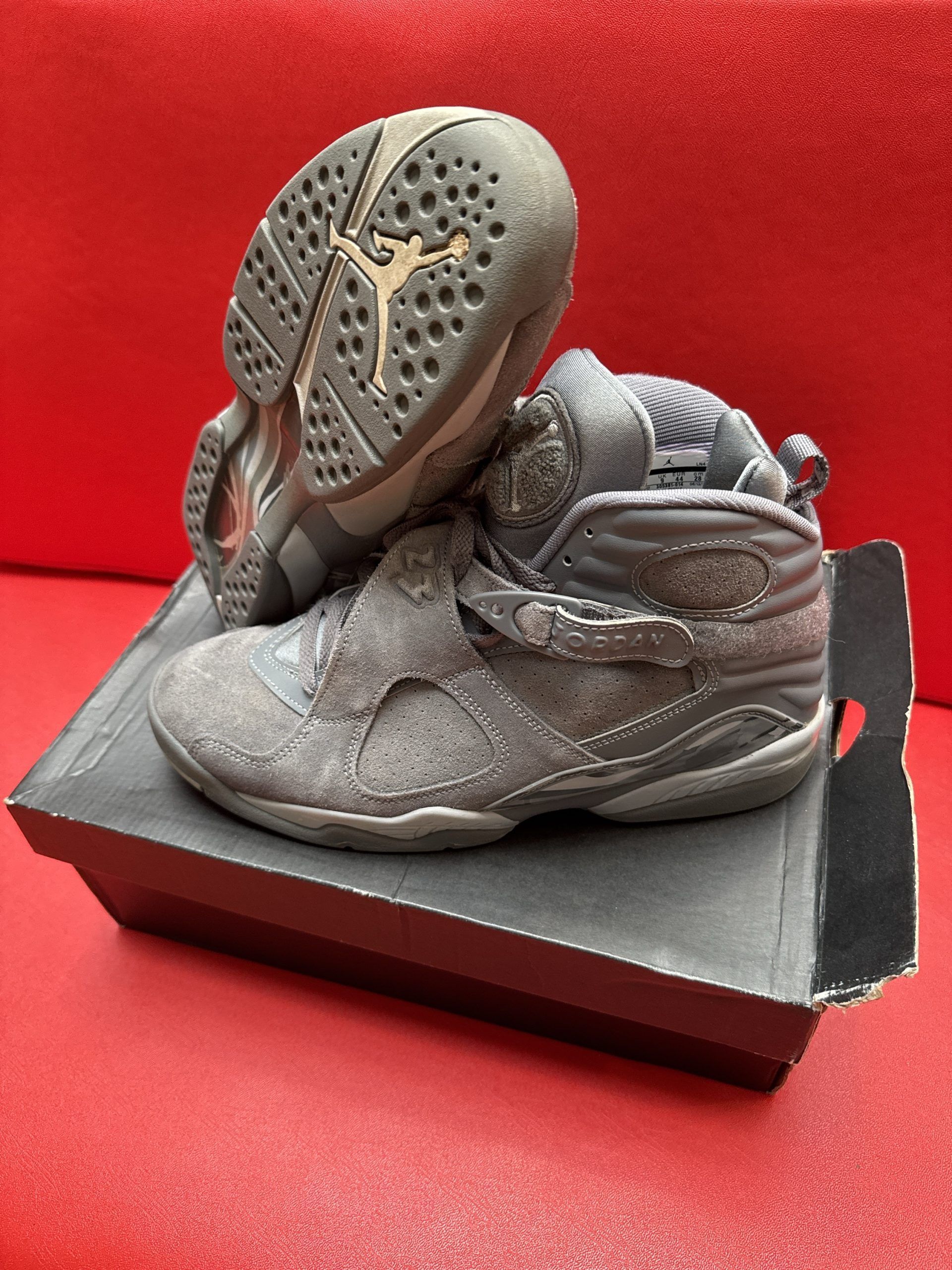 Gray Air Jordan 8 sneakers on a black shoe box against a red background.