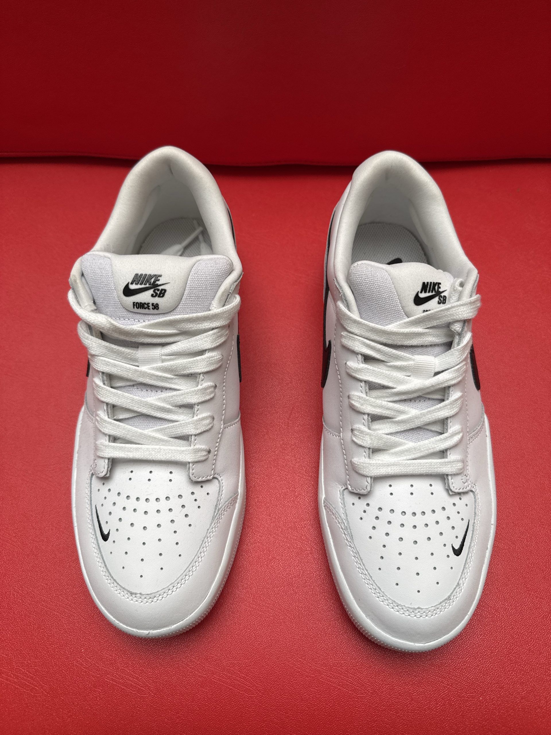 White Nike sneakers with black swoosh on red surface. One shoe is flipped to show the sole.