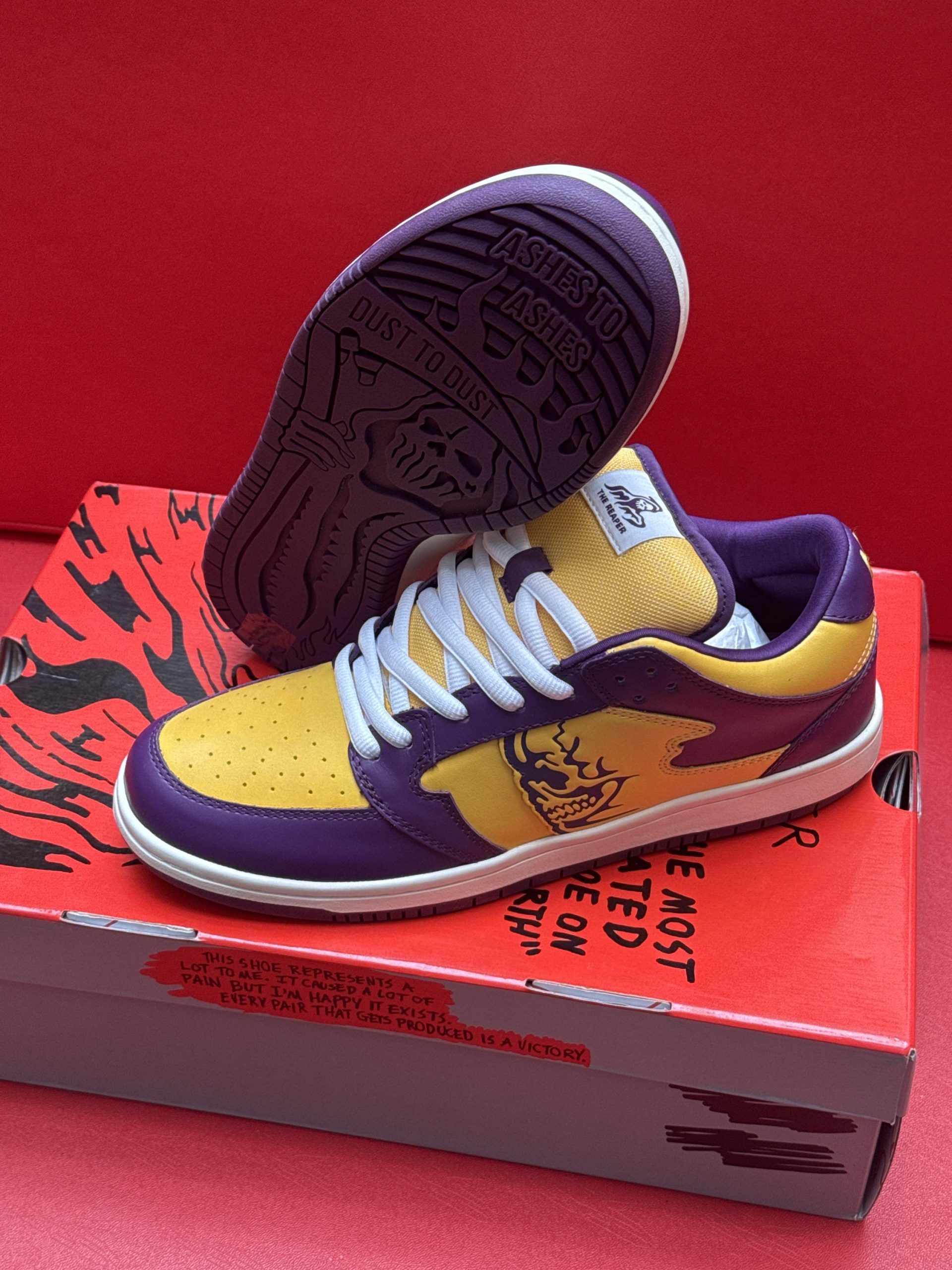Purple and gold sneakers with a logo on a red patterned shoebox against a red background.