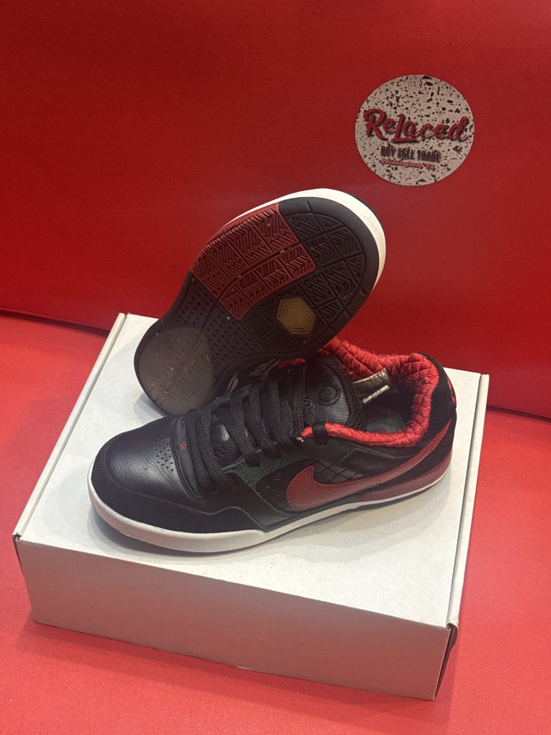 Black Nike sneakers with red accents, on a white box against a red backdrop.