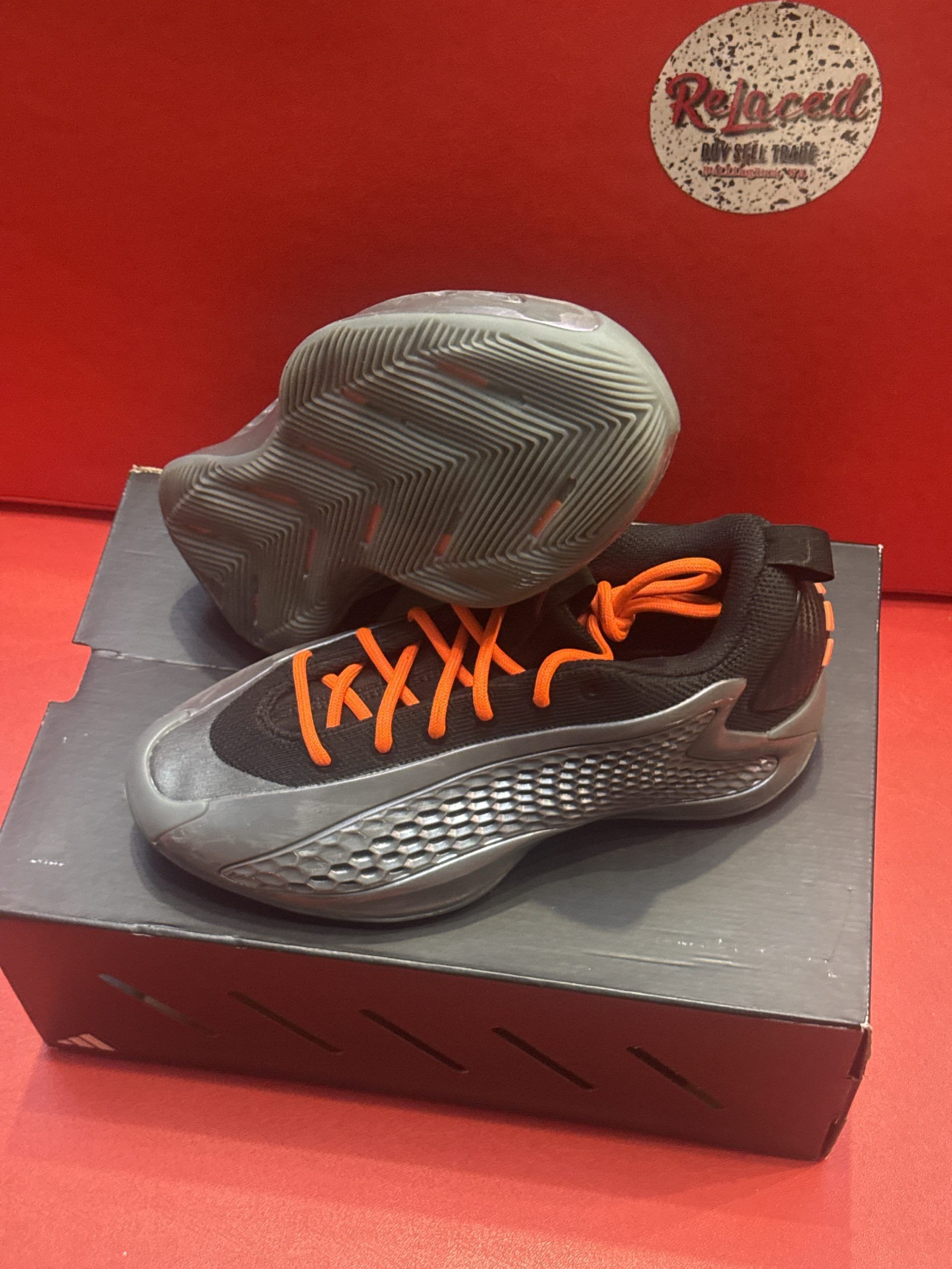 Black and orange sneakers sit on a dark box against a red background. One sneaker is flipped over.