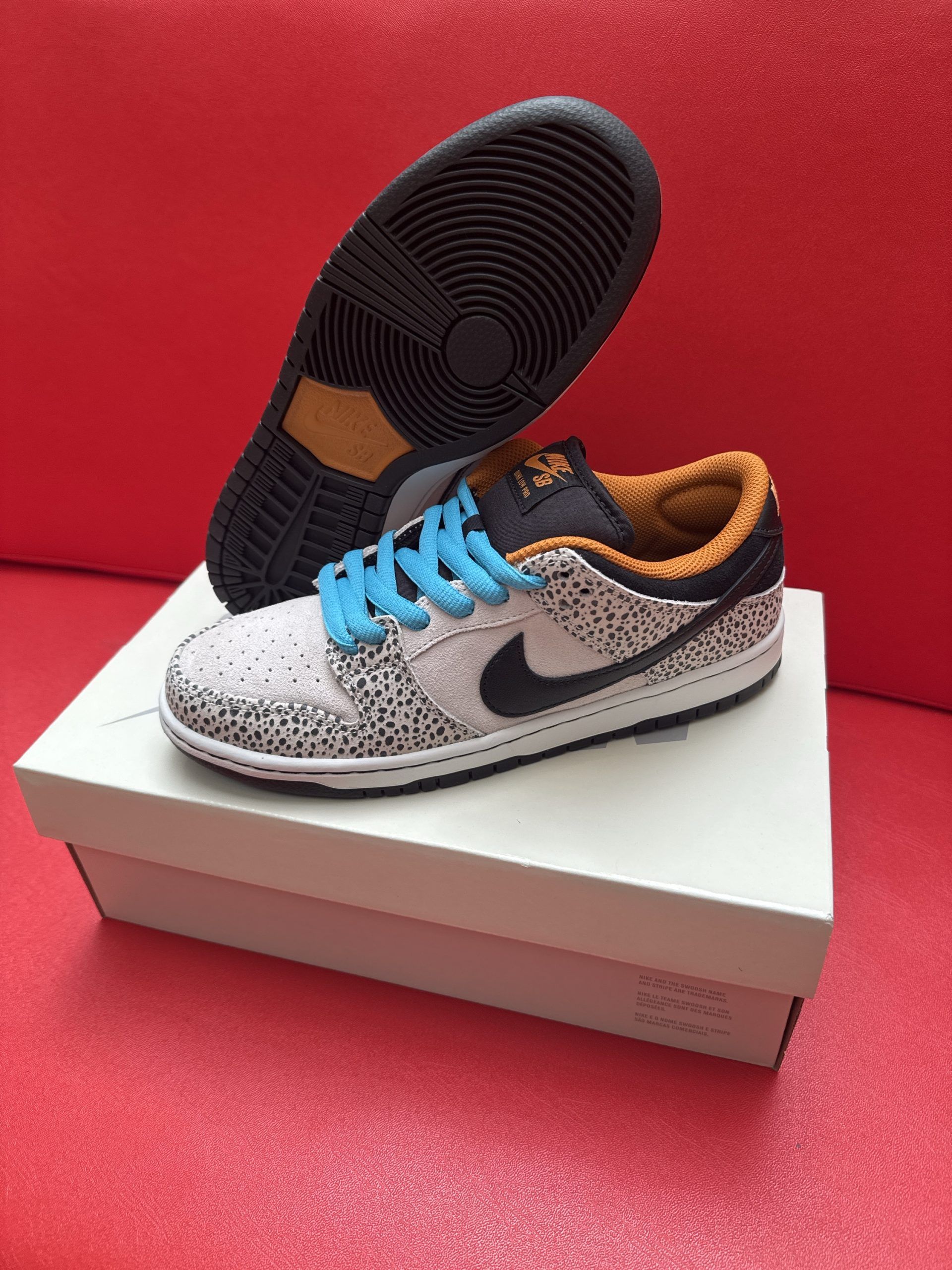 Nike Dunk Low sneakers with blue laces, spotted design, and black sole, displayed on a white box against a red background.