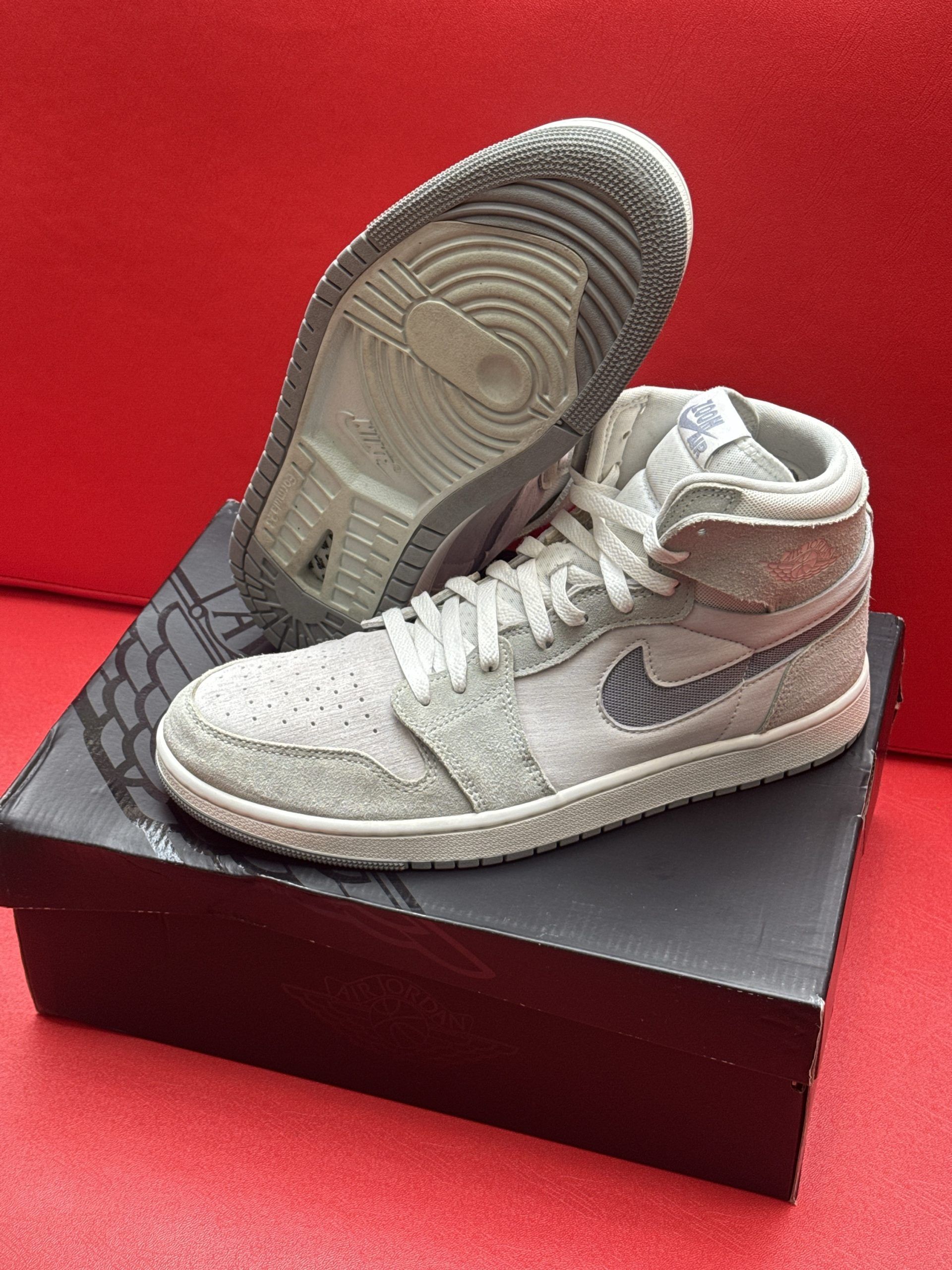 Pair of gray and white Air Jordan sneakers on top of a black shoebox, sole up.