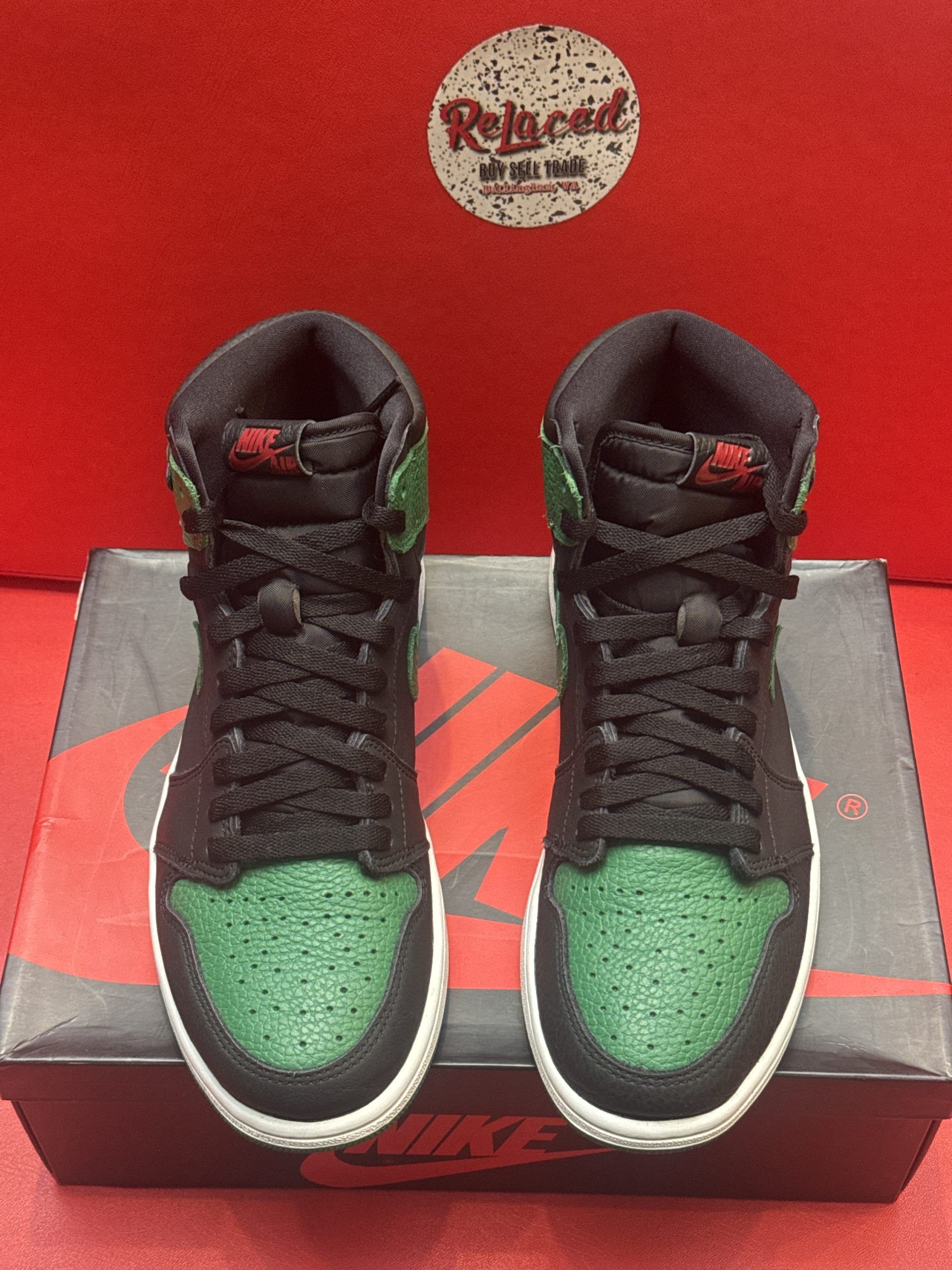 Green and black Air Jordan 1 sneakers on a box, red background.