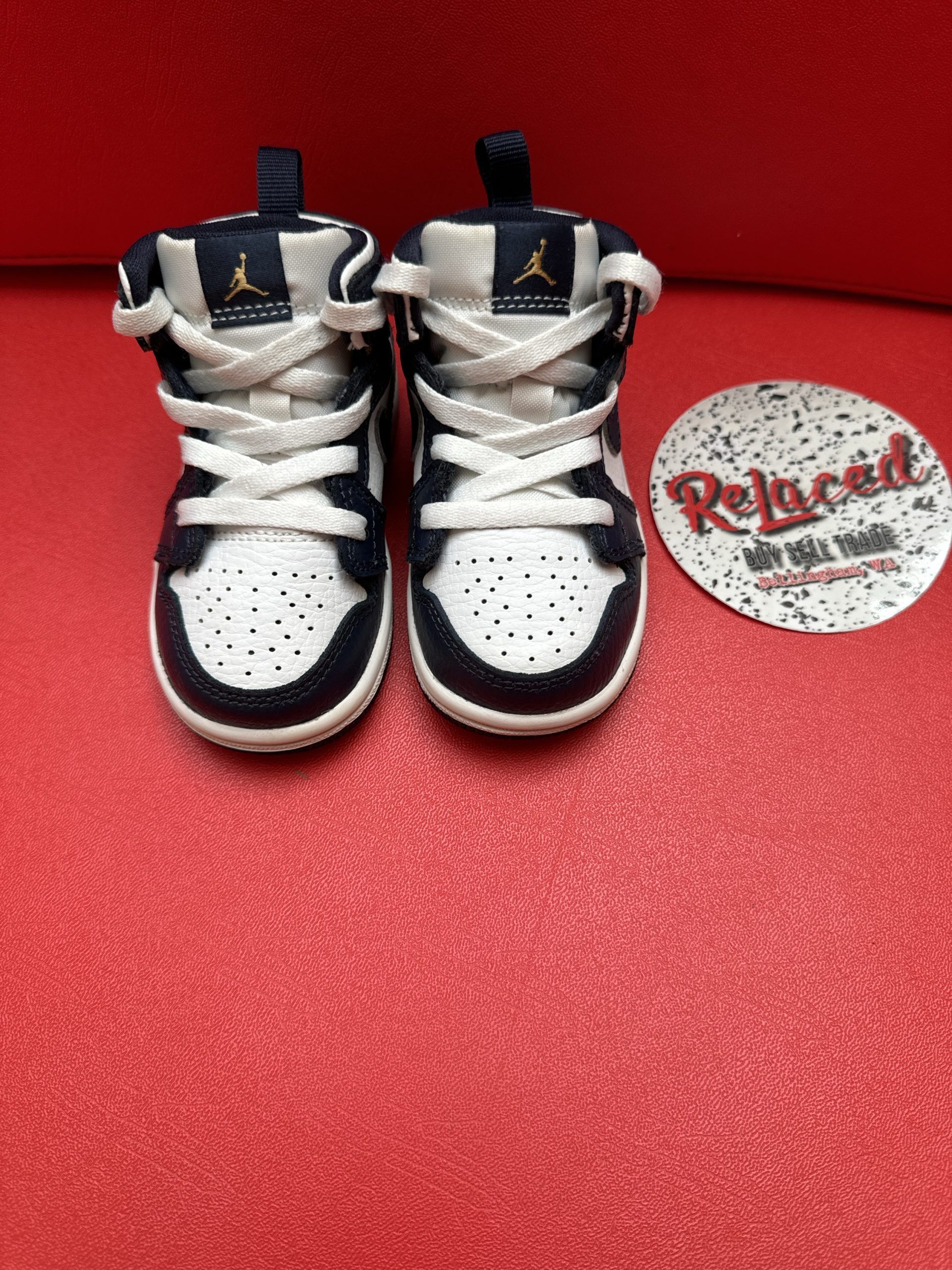 Pair of black and white toddler Air Jordan 1 sneakers on a red surface.